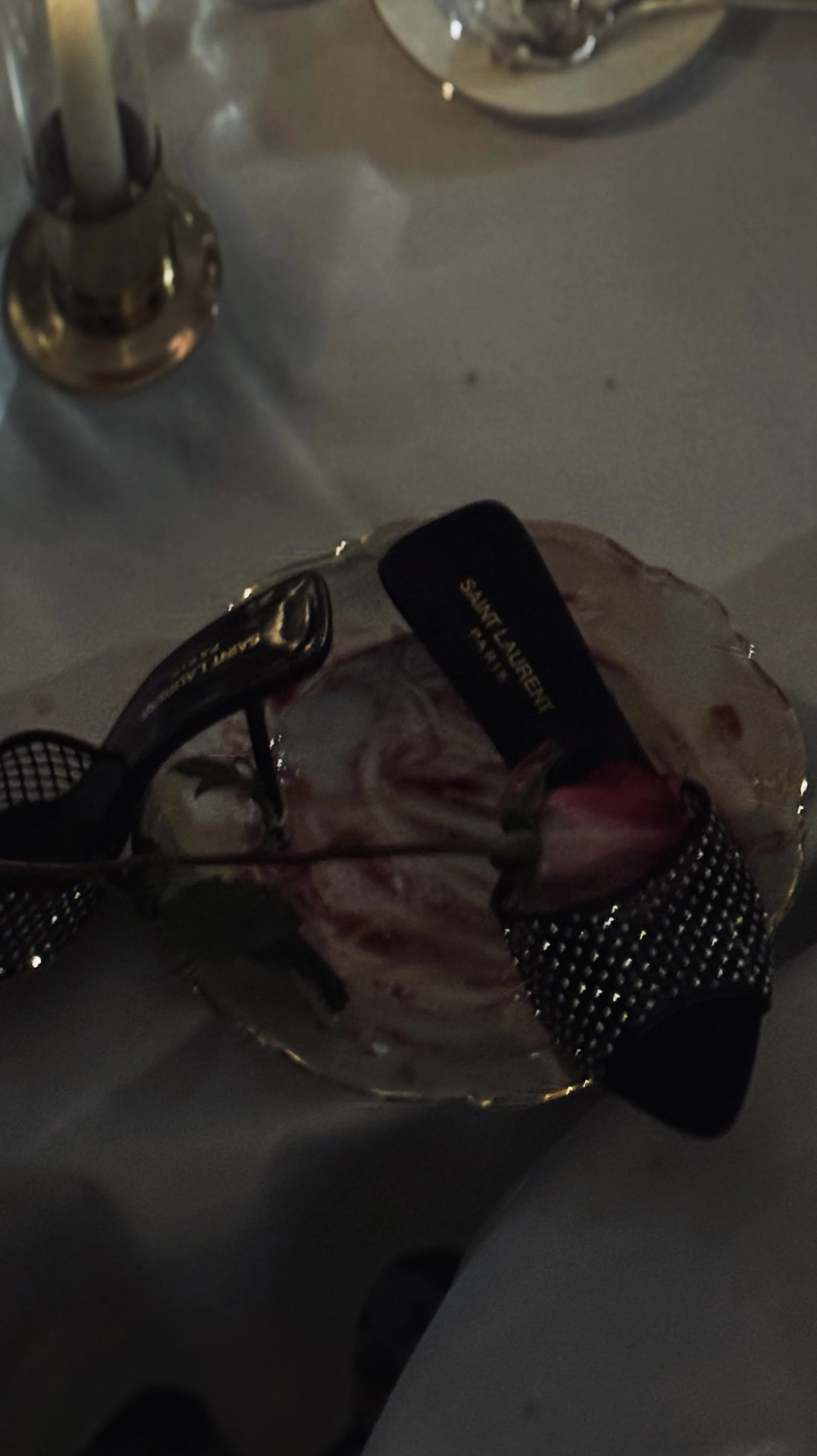 A dessert with swirled pink and white marbled cream, garnished with a raspberry and a small green leaf, served in a clear glass dish with a black label on top.