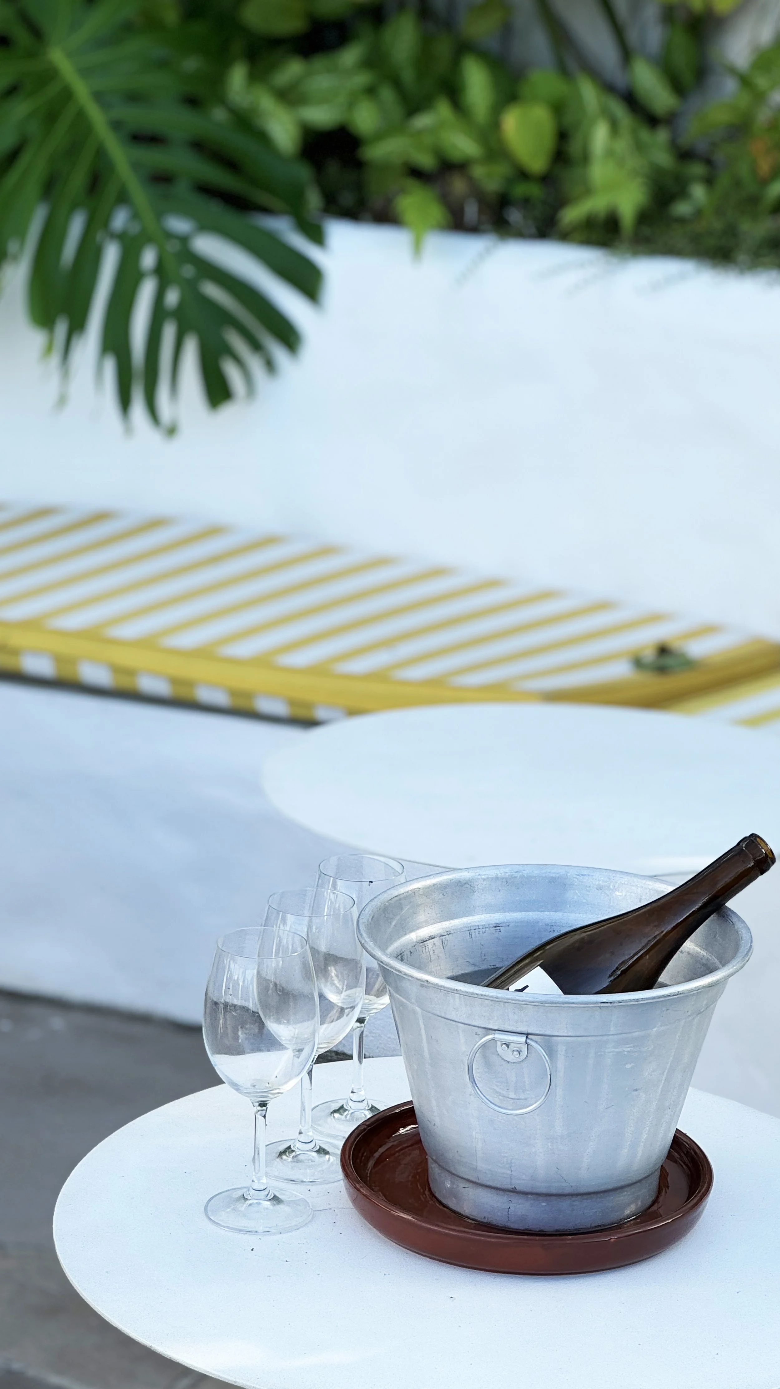 A table with four empty wine glasses and a bottle in a metal ice bucket on a terracotta tray on a round white table.