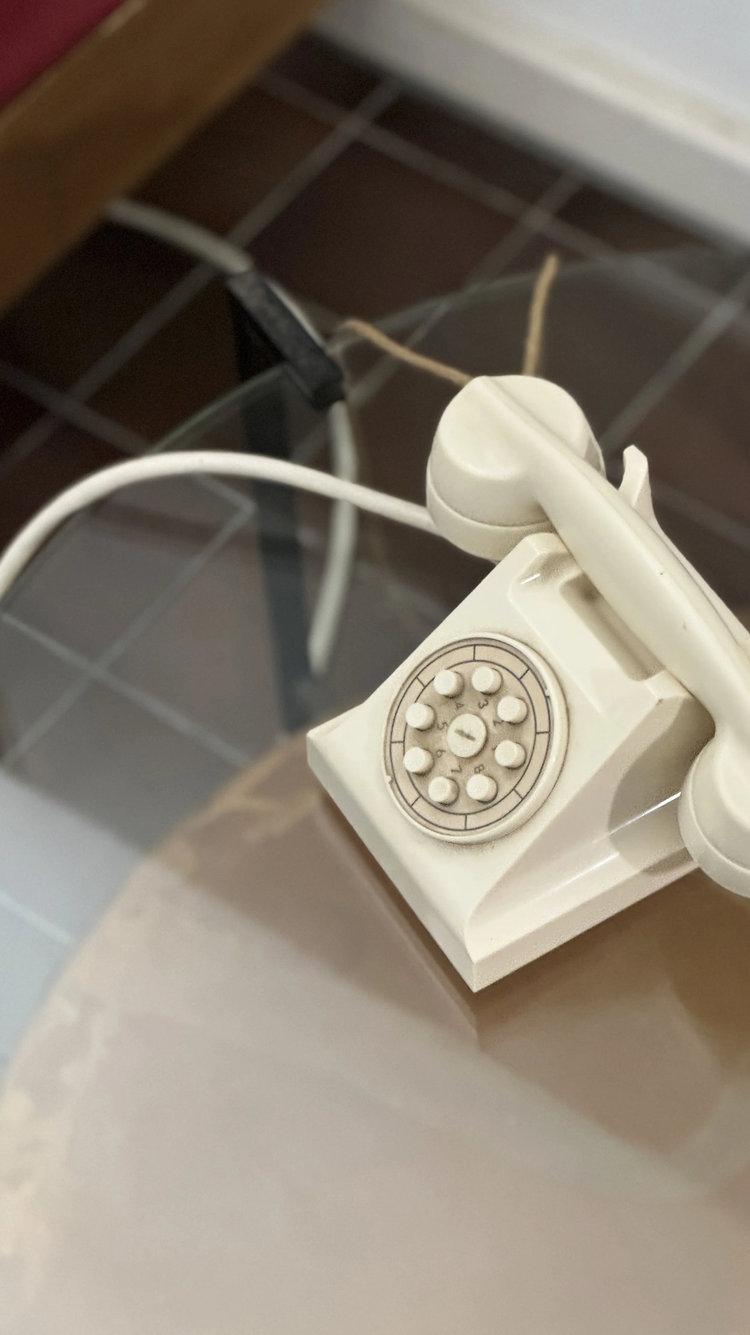 Close-up of a vintage rotary dial telephone on a table with a tiled wall in the background.