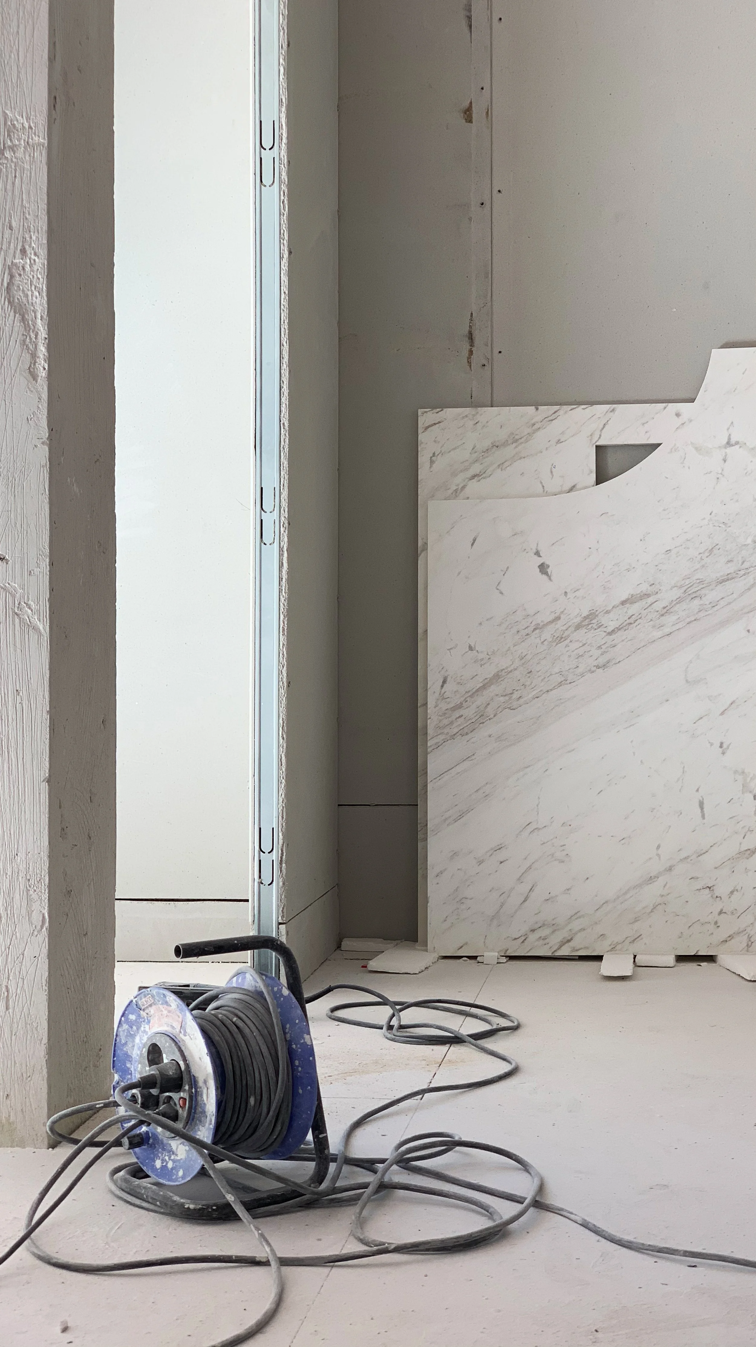 Construction site with a coiled extension cord and some marble tiles leaning against the wall.