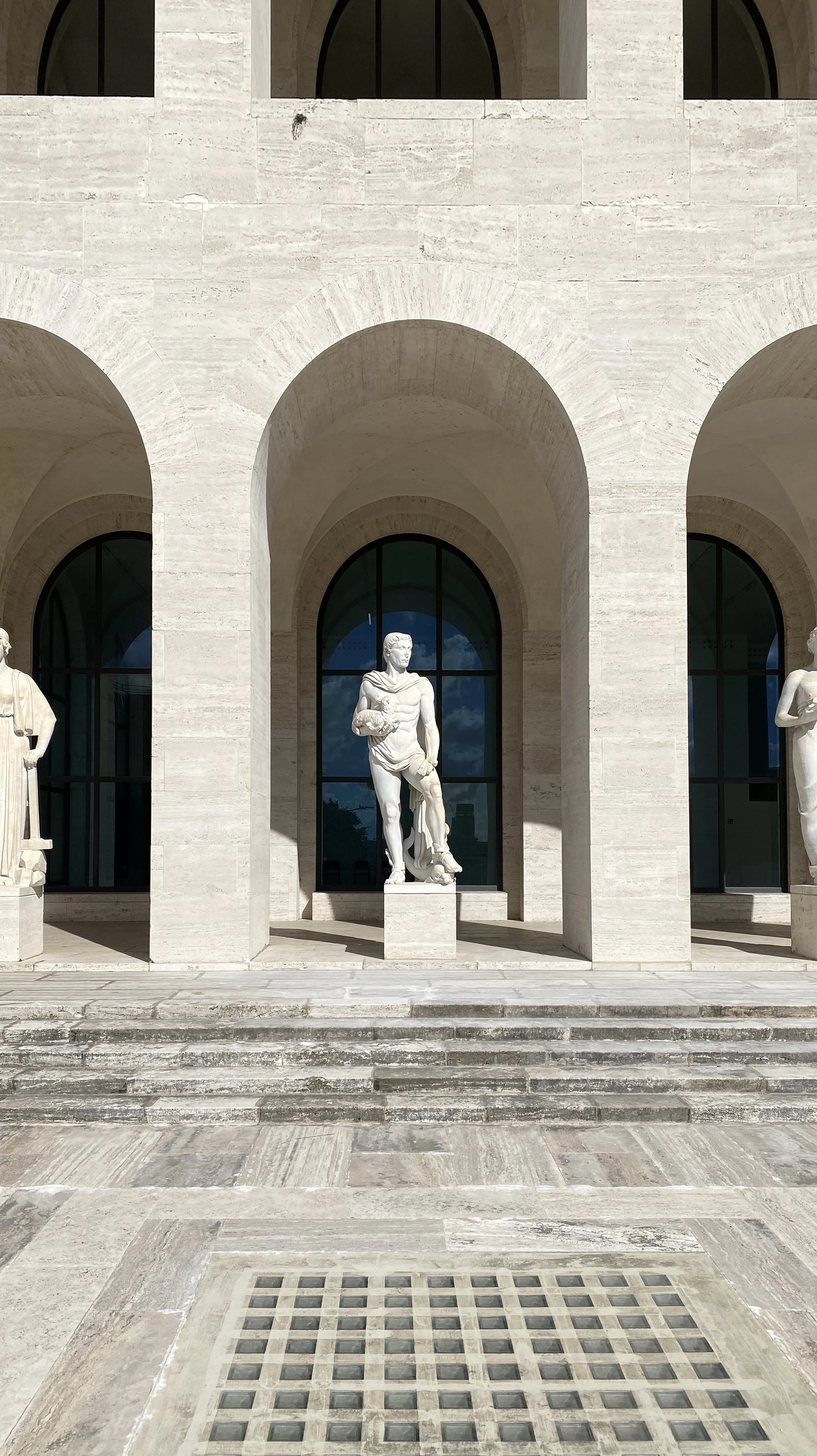 Benjamin Liatoud Architect designs sophisticated residential and hospitality projects. Statues of classical sculptures on a marble building with large arched windows and steps in front in Roma, Italy.
