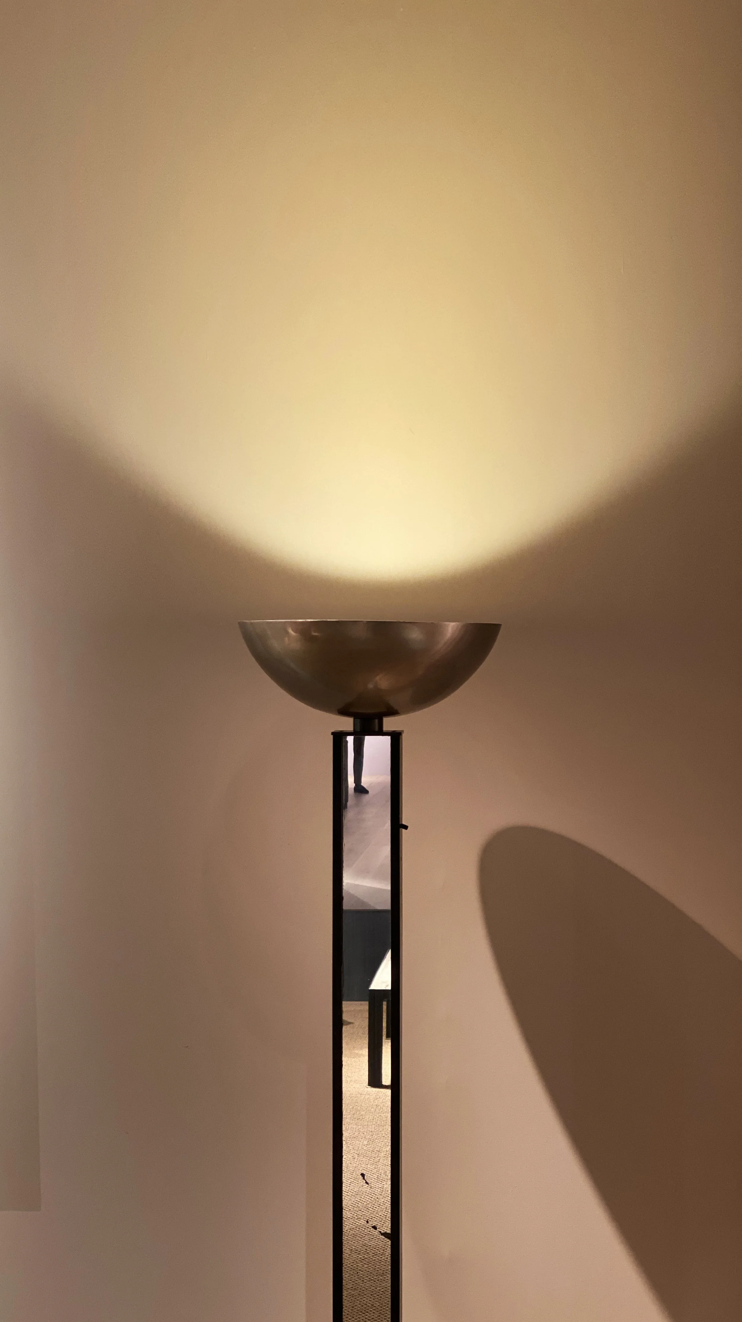 Benjamin Liatoud is a global architect and art director crafting high-end residential, hospitality and commercial spaces. A floor lamp with a metallic bowl-shaped shade casting a warm glow onto the wall.