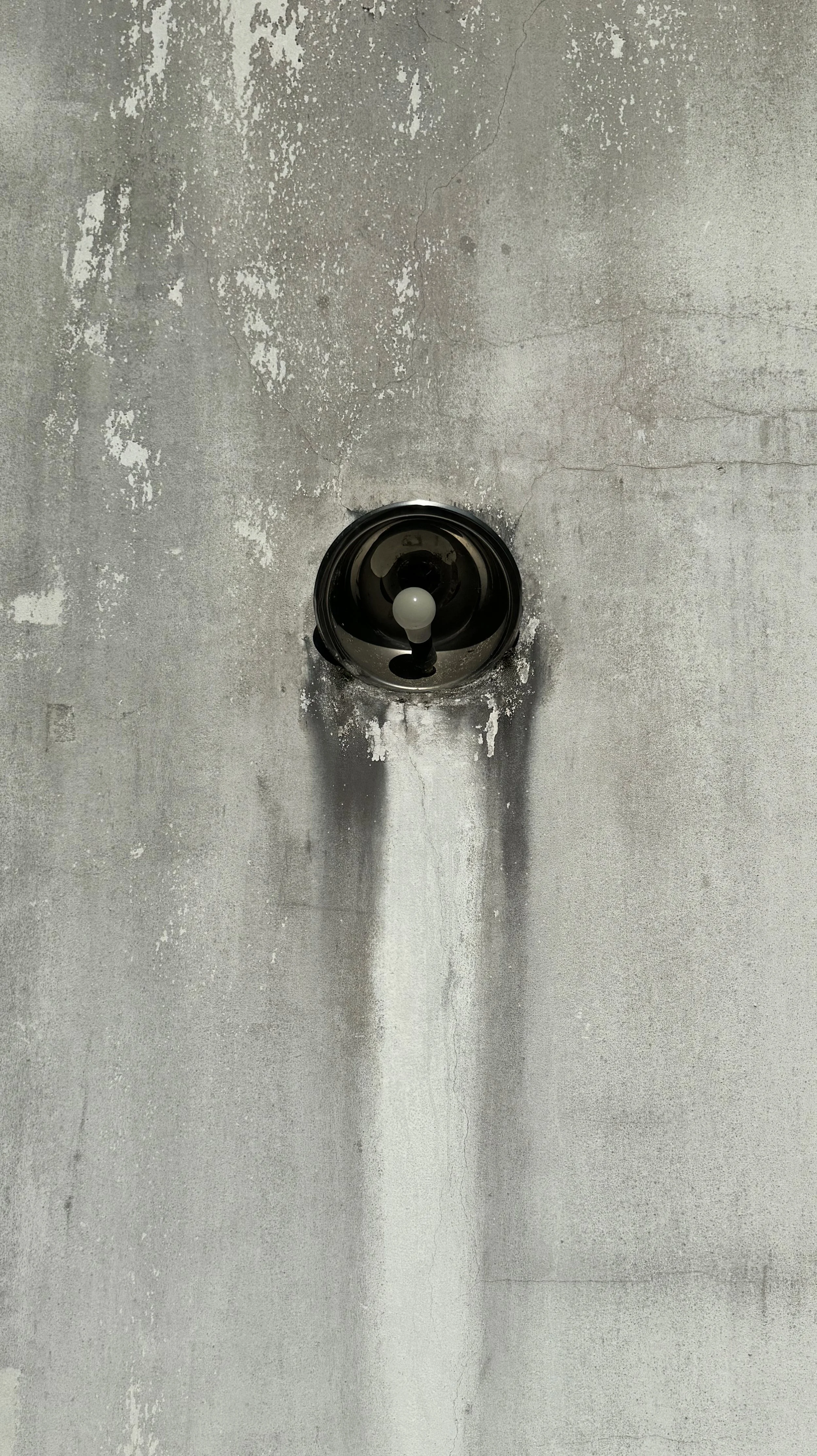 Benjamin Liatoud designs bespoke luxury architecture worldwide. Ceiling with a single light bulb fixture and stained, cracking paint on the surrounding wall.