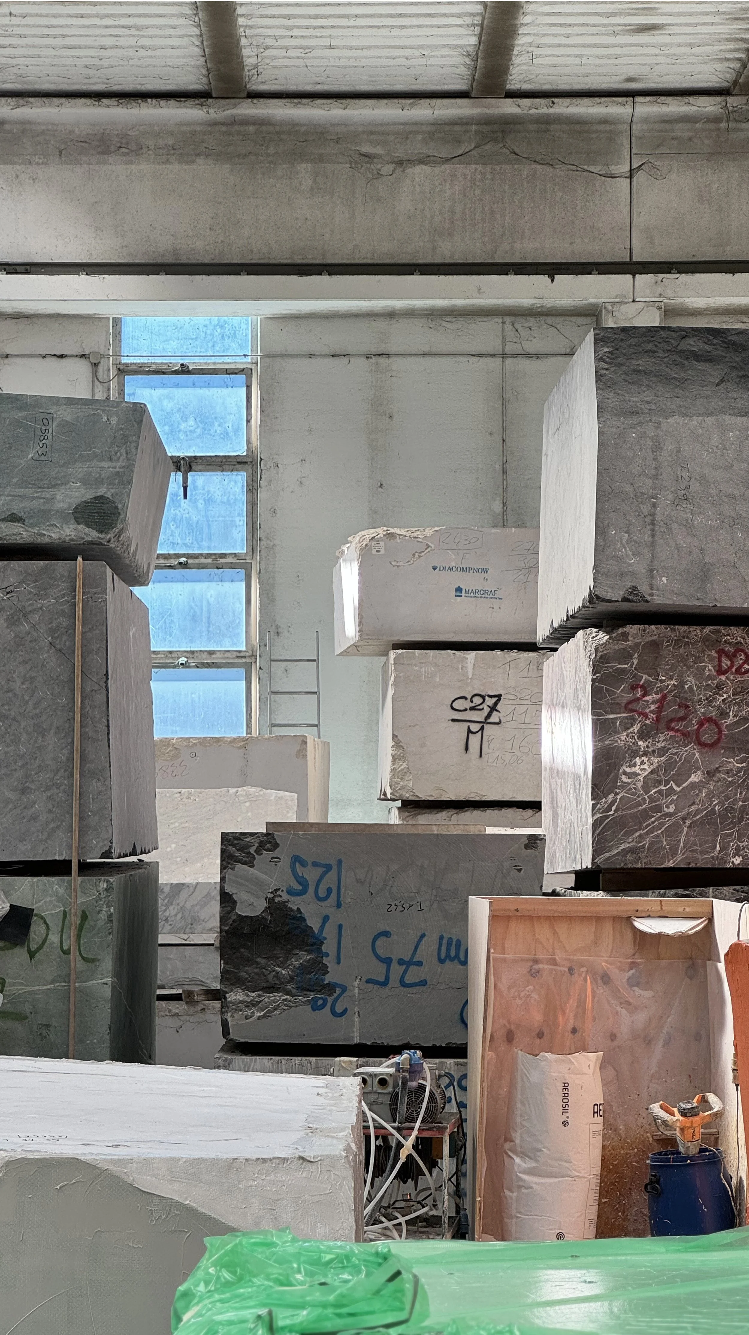 Interior of a marble or stone warehouse with large blocks of stone stacked on top of each other, some with markings and labels.