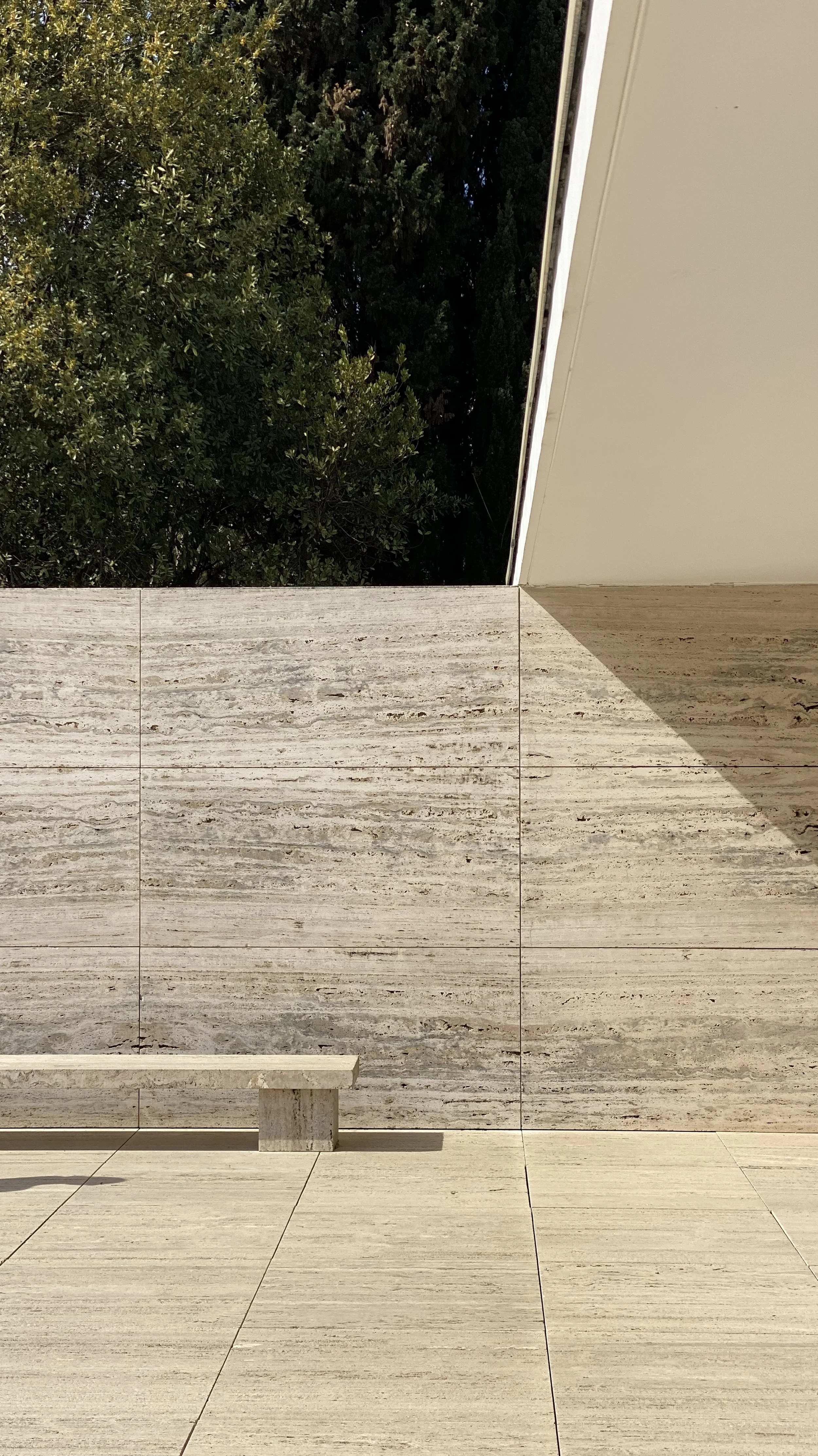 Photo of a beige stone wall and floor with a white ceiling, and green trees visible in an opening.