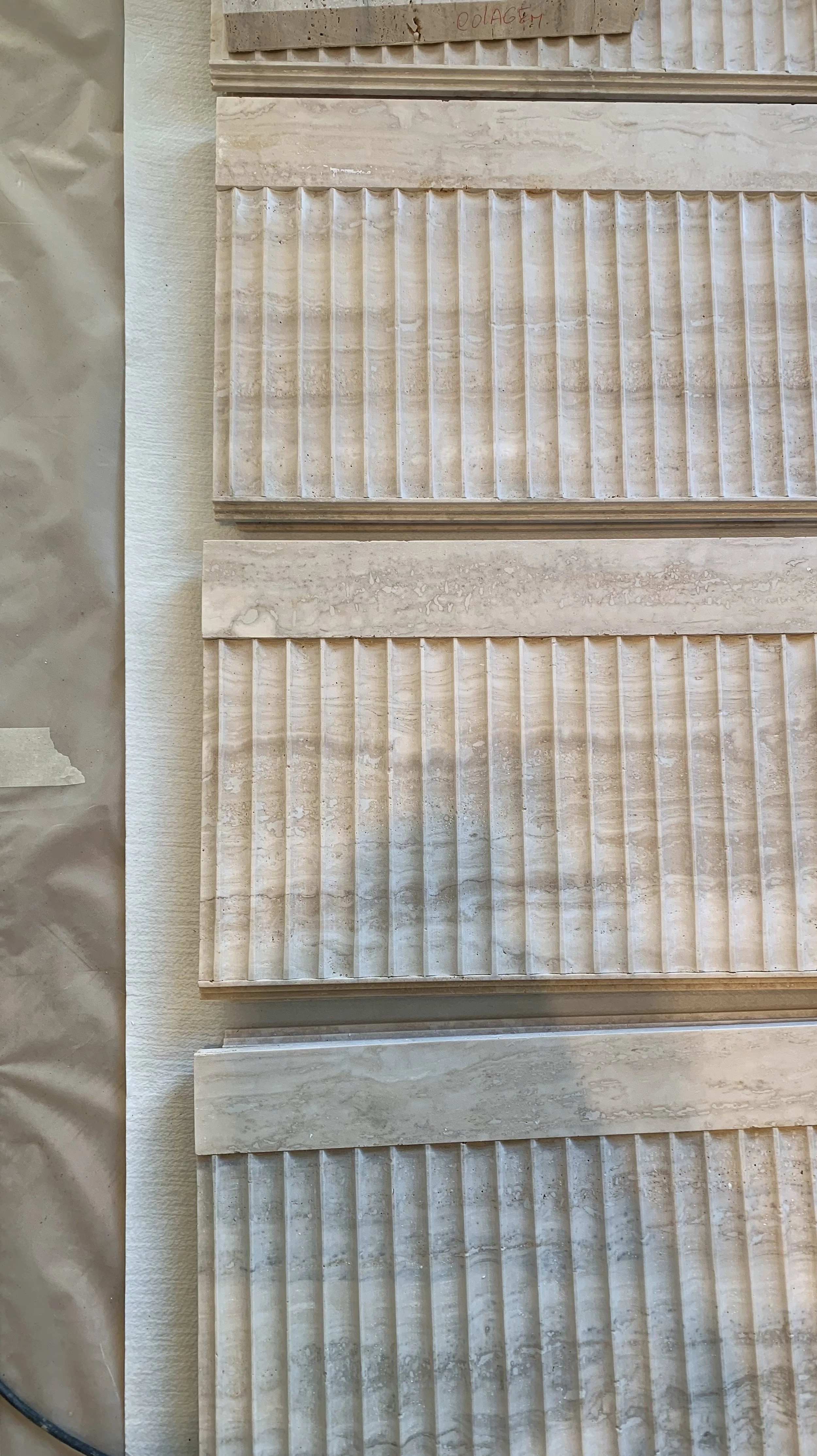 Approximately eight rectangular beige wall tiles with textured, grooved patterns stacked vertically.