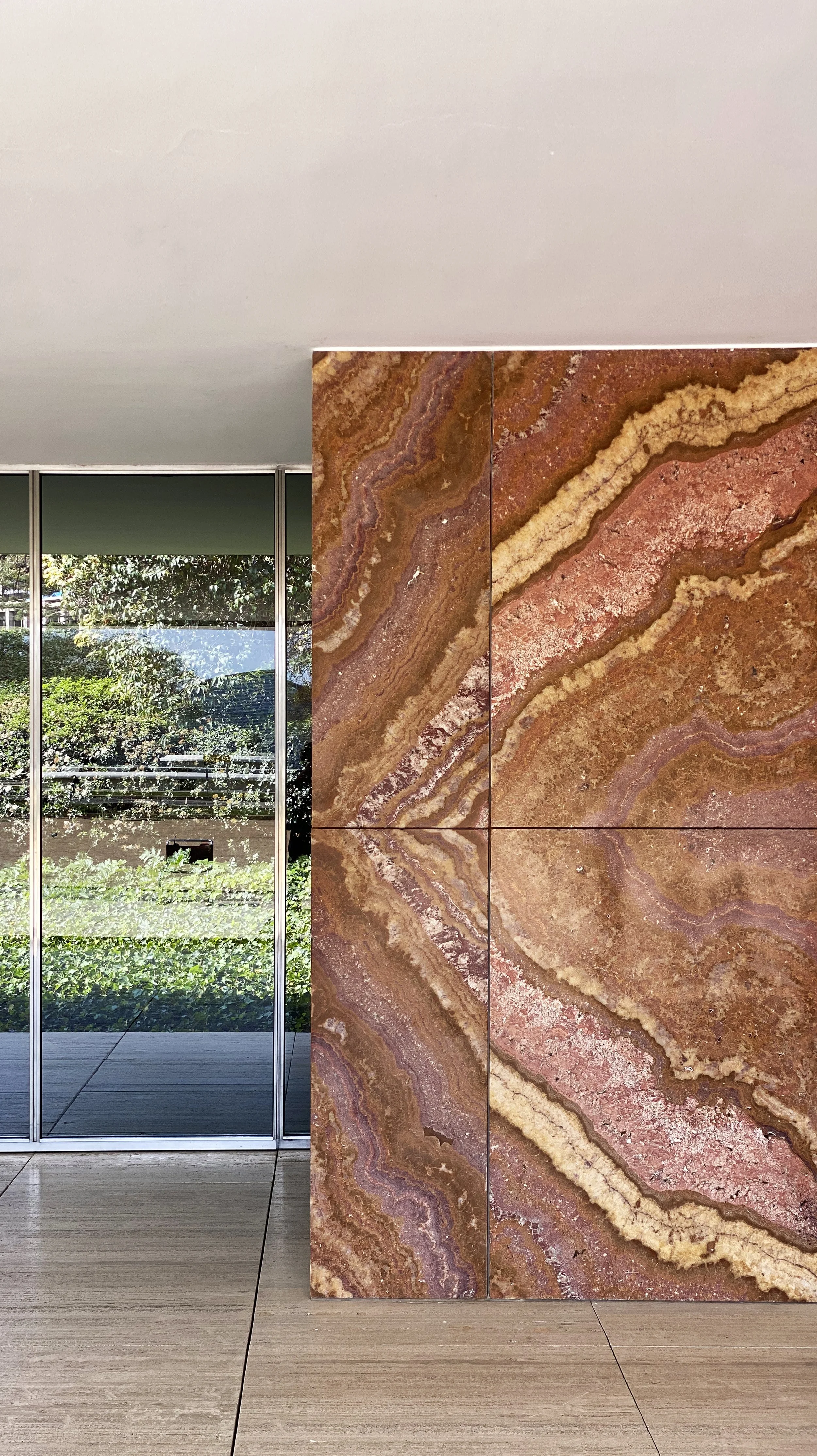 Interior view showing a large stone wall with natural red, pink, and brown veining, beside a glass sliding door overlooking a lush green garden.