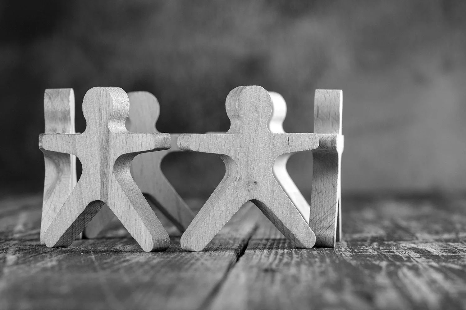 Three wooden figures holding hands in a circle on a wooden surface with a blurred background.