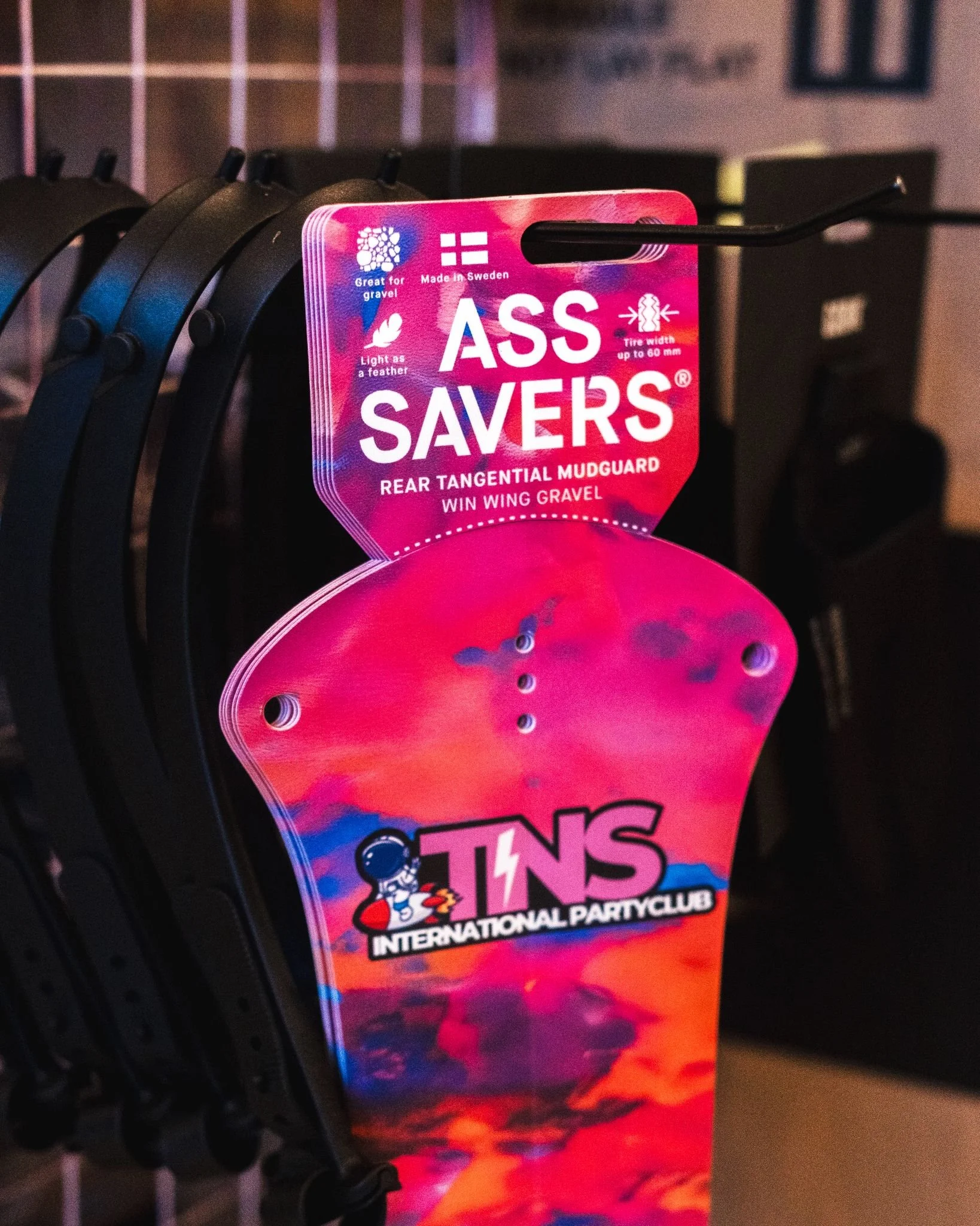 Een fietsonderdeel in de winkel, met een opvallend roze en blauwe verpakking waarop staat 'ASS SAVERS' en 'REAR TANGENTIAL MUDGUARD WIN WING GRAVEL'.