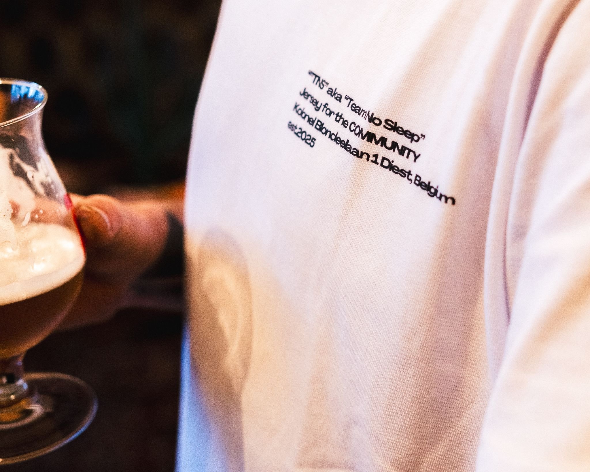 Close-up van een witte trui met tekst en een persoon die een glas bier vasthoudt.
