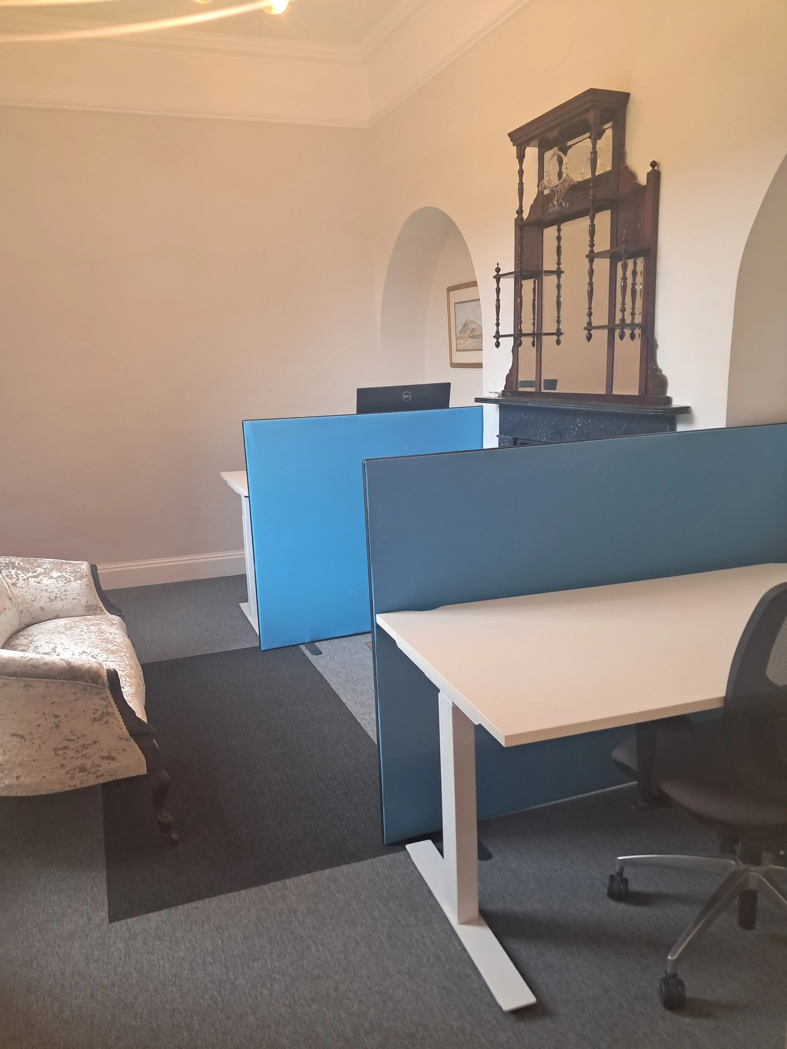Office with desks, blue privacy panels, black office chair, vintage armchair, and wooden wall decor.