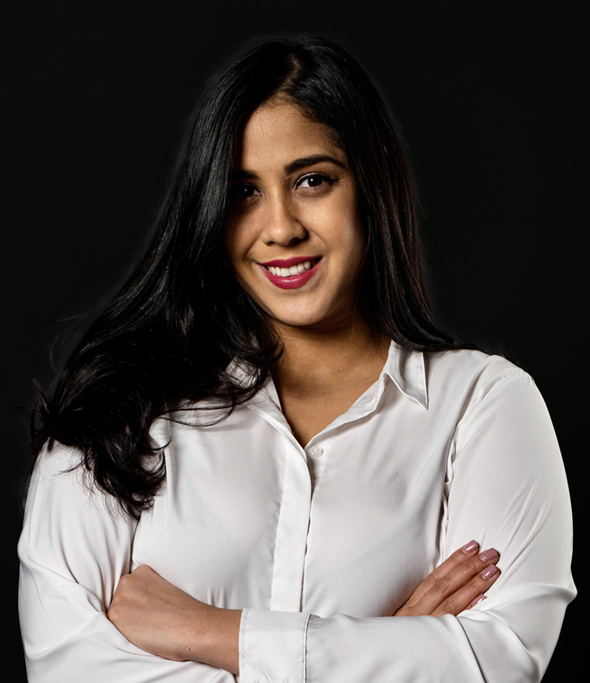 A woman with long dark hair and a white blouse standing against a black background, smiling and crossing her arms.
