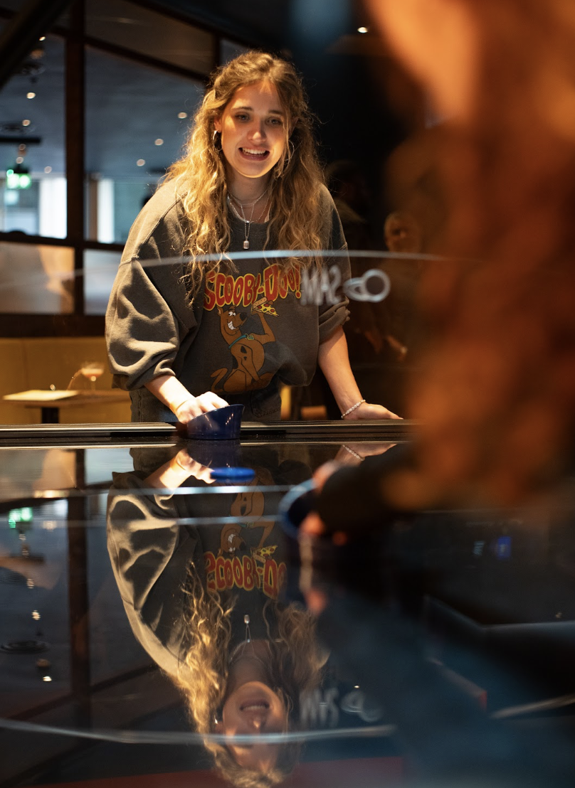 Image of a black air hockey table and a girl pushing a blue puck 