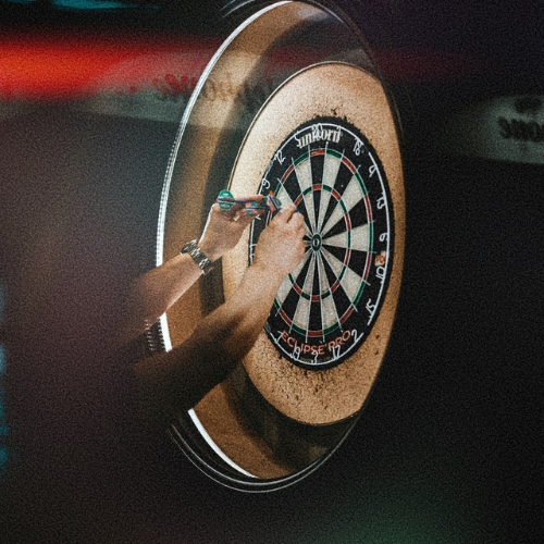 A person playing darts on one of The Lucky Goats epic tech dartboards. They probably just scored a bullseye. So I'm afraid it's your round.