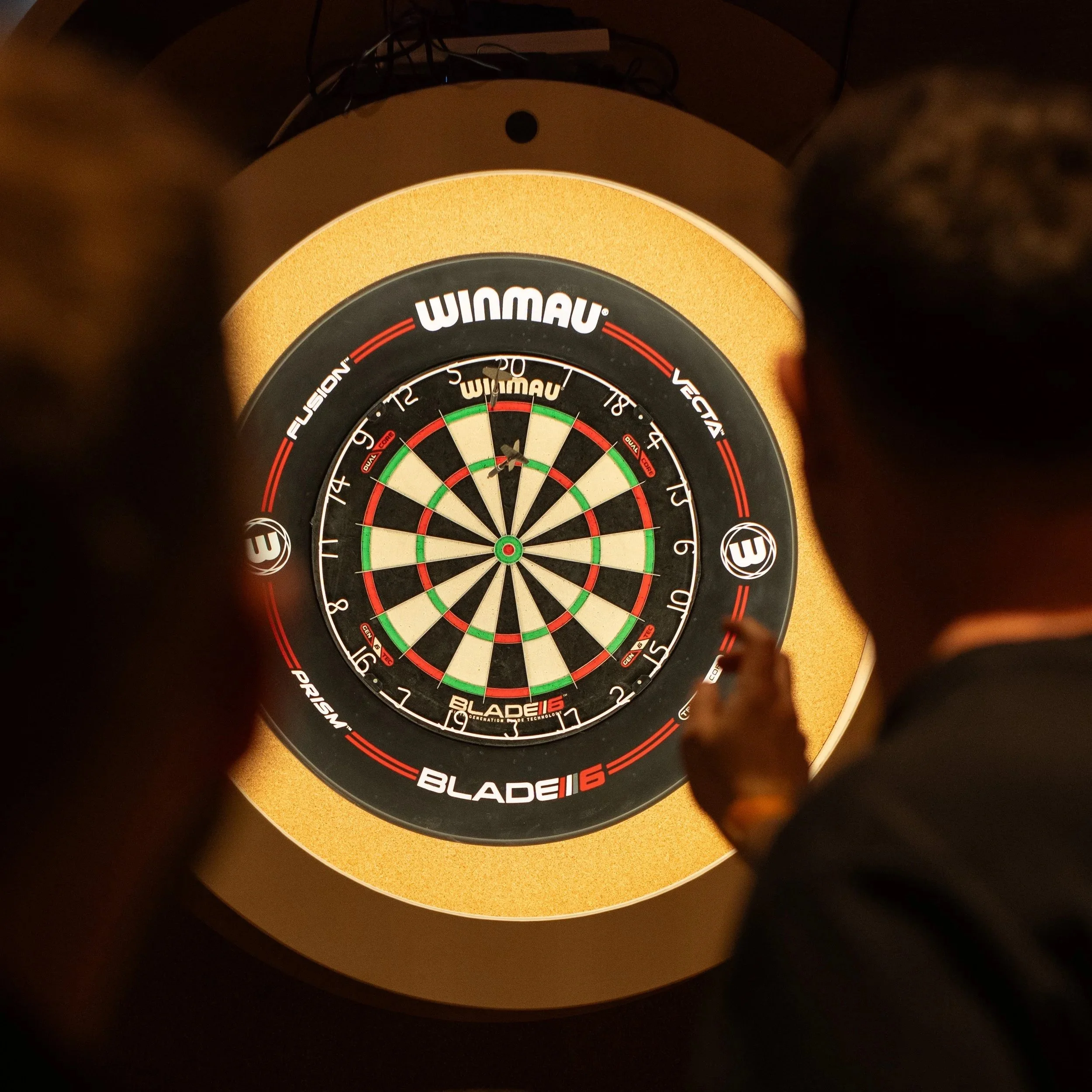 A person playing darts on one of The Lucky Goats epic tech dartboards. They probably just scored a bullseye. So I'm afraid it's your round.