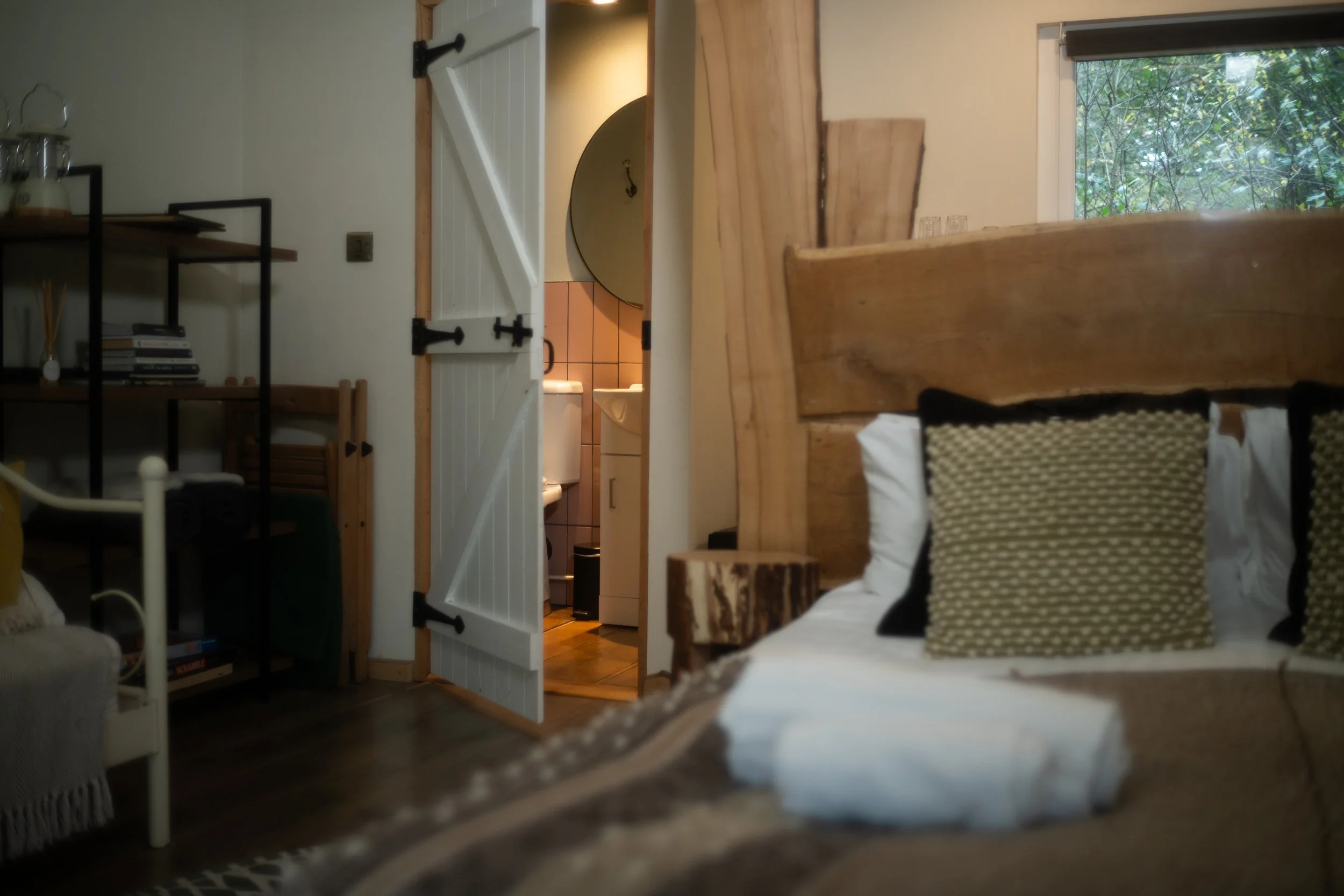 Interior of a cozy room with a bed, pillows, and a view into a bathroom with pink tiles and a round mirror.