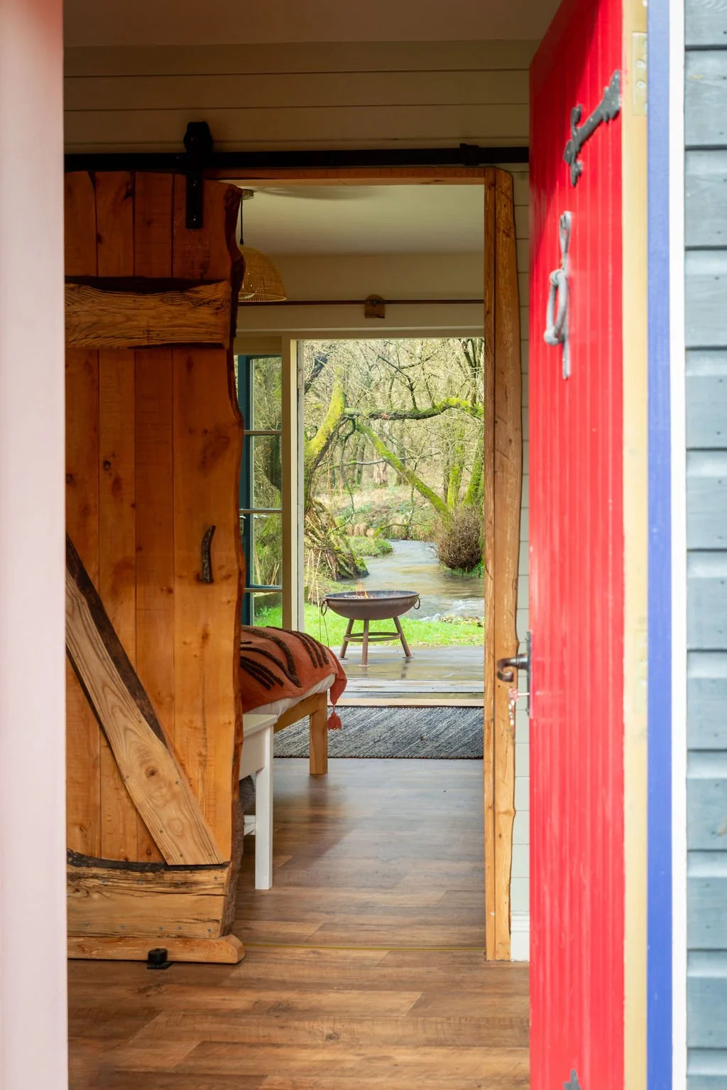View through doorway showing rustic interior with wooden furniture and a view of trees and a small stream outside.