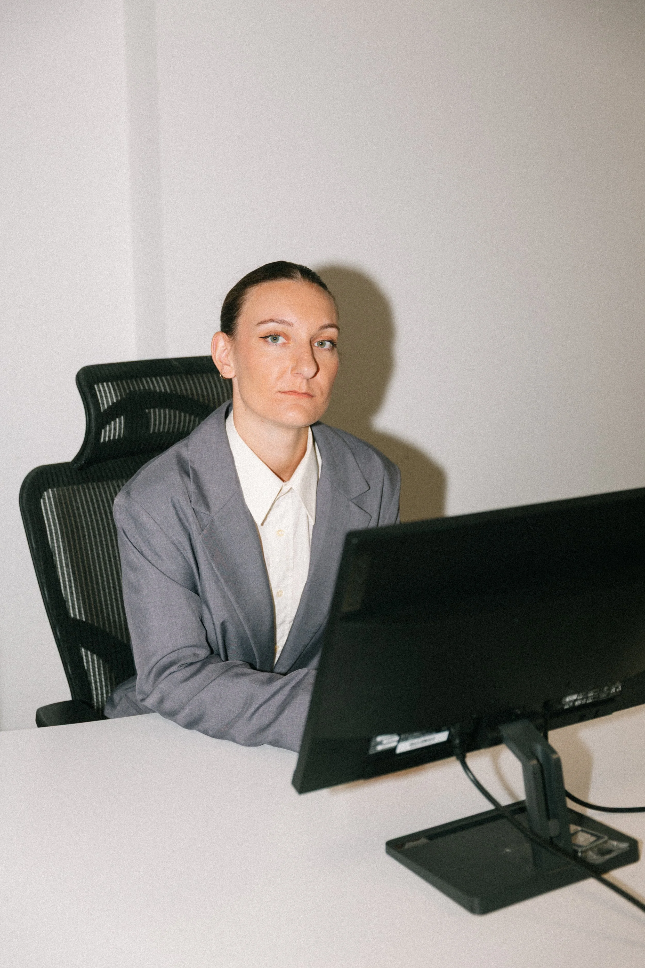 "Une femme d'affaires assise à un bureau, portant un costume gris, regarde l'appareil photo, avec un fond gris clair." j'aime bien la description générée, je garde