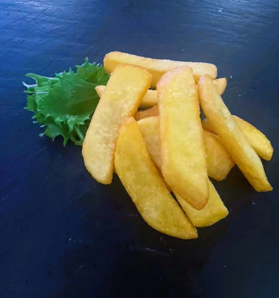 Frittierte Kartoffelspalten mit grüner Salatblatt auf einem schwarzen Teller.