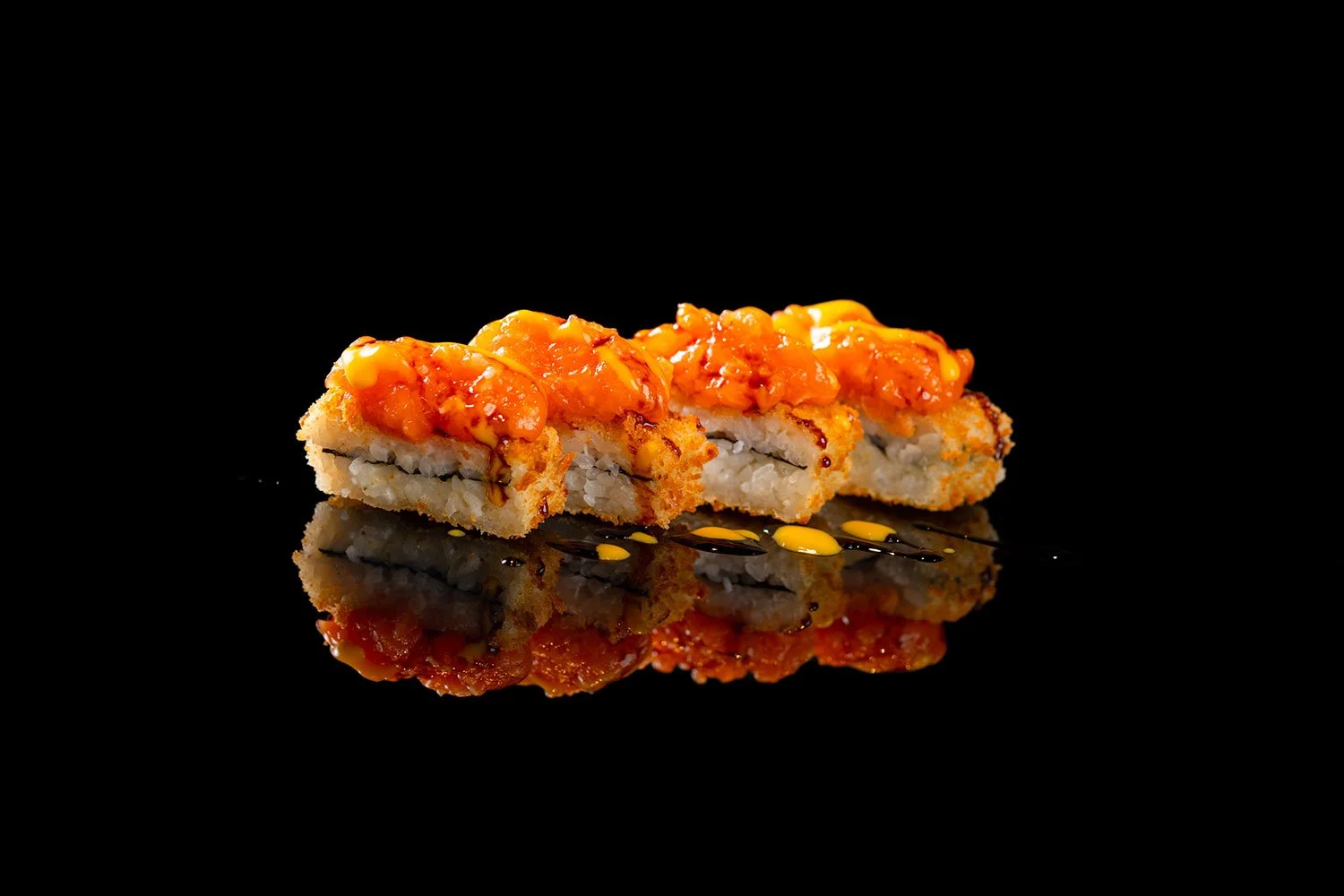 Sushi mit einer fruchtigen orangenen Sauce auf einem schwarzen Hintergrund, mit Reflexion auf der Oberfläche.