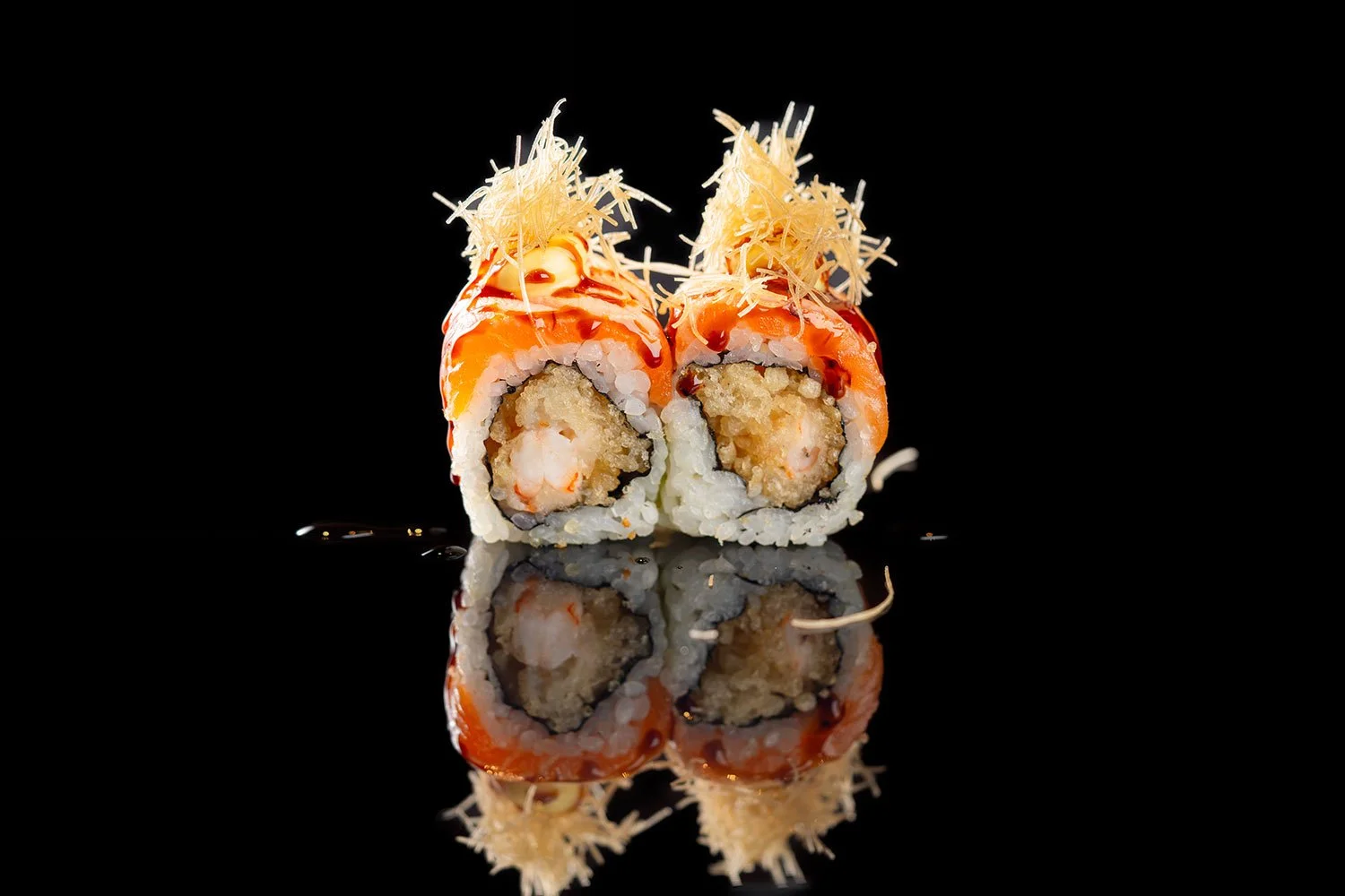 Zwei Sushi-Rollen mit Lachs, Garnelen, Reis, Nori-Blatt, Toppings aus Parmesan und einem dunklen Soßen-Drizzle auf schwarzem Hintergrund mit Spiegelung