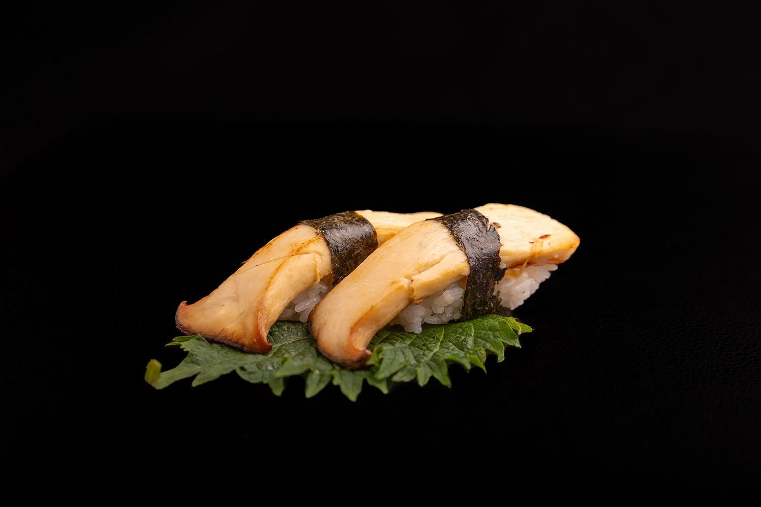 Sushi mit vier Stück, Seetang umwickelt, auf einem grünen Blatt, schwarzer Hintergrund.