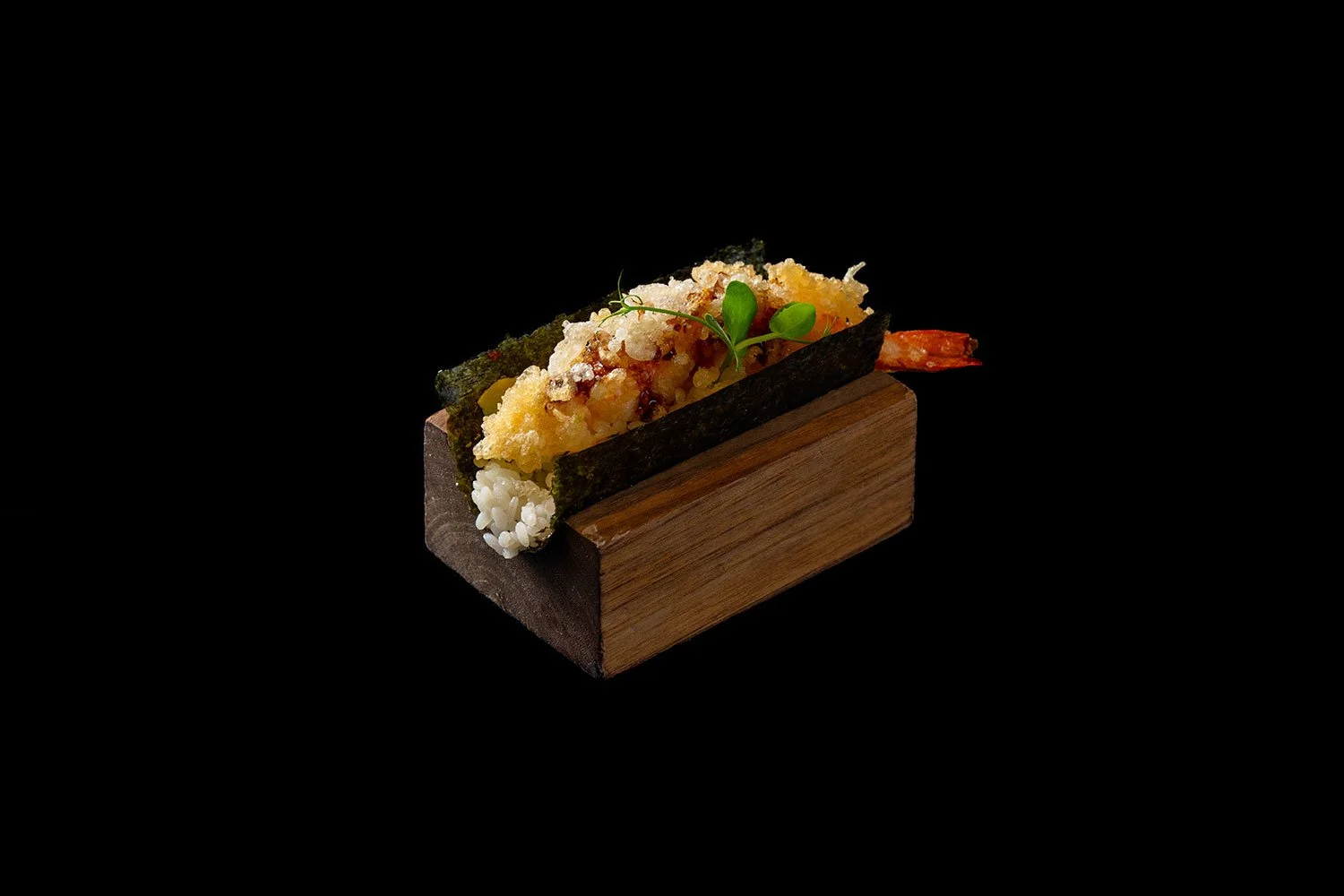  Sushi auf Holzblock, mit Tempura-Garnelen, Nori-Blatt, Reis, und grüner Dekoration, schwarzer Hintergrund.