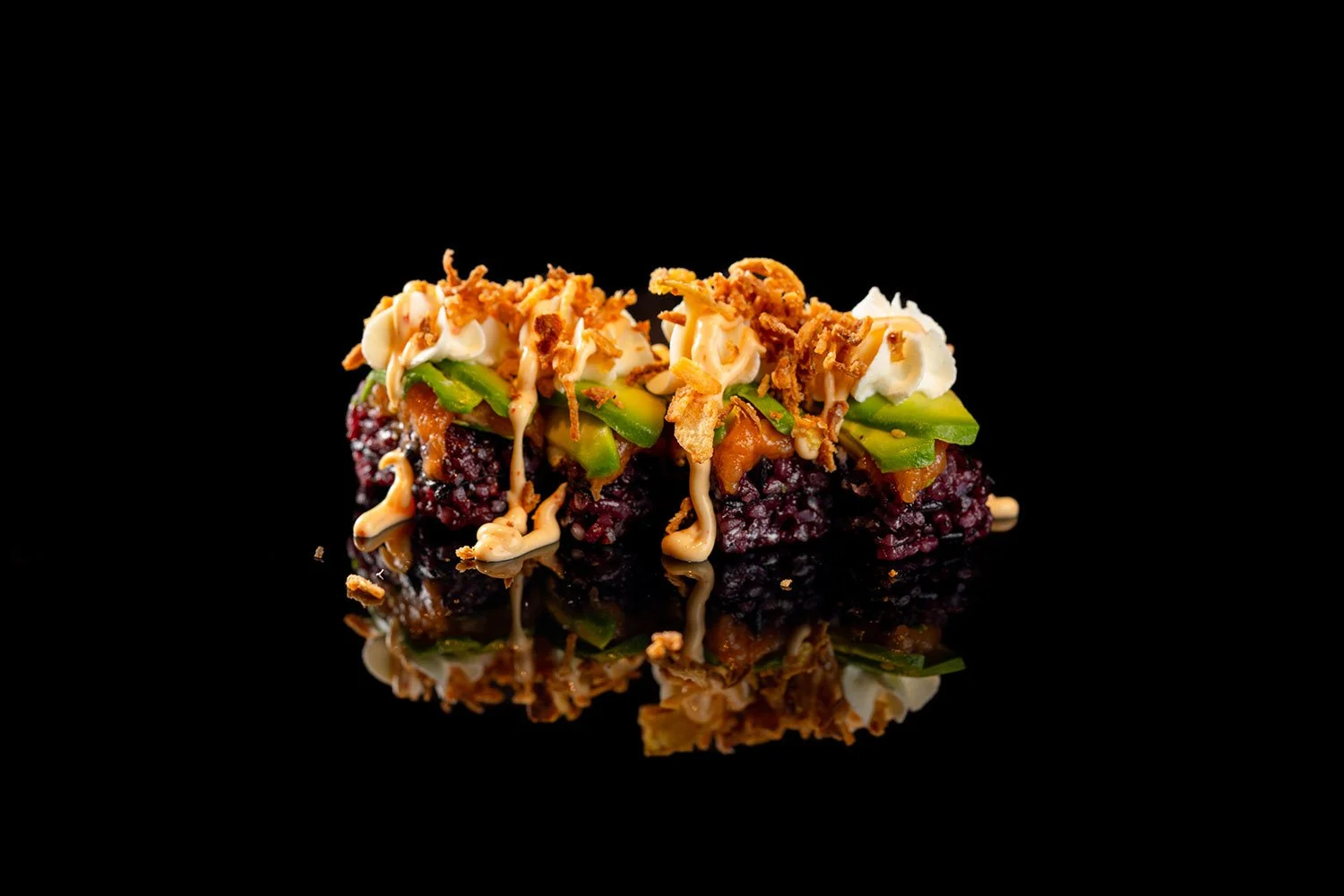 Sushi mit schwarzen Reis, Avocado, Frühlingszwiebeln, Mayonnaise und knusprigen Zwiebeln auf schwarzem Hintergrund mit Reflexion