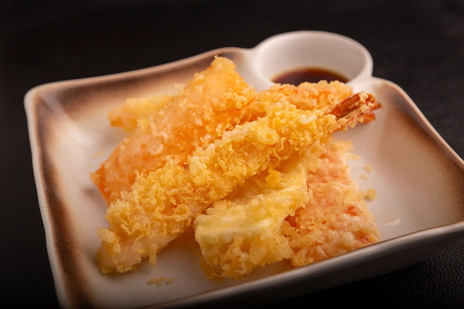 Knusprige Tempura-Garnelen mit Dip-Sauce auf einem weißen Teller.