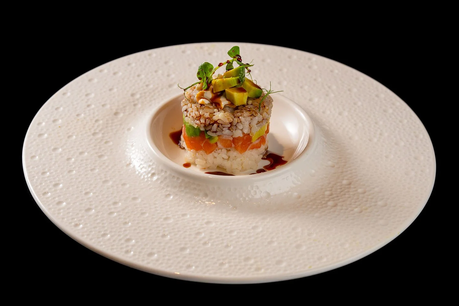 Kleines, gericht mit geschichtetem Sushi-Art-Insid auf silbernem Teller, mit Avocado, Karotten, Reis, und Sauce, dekorativ garniert.