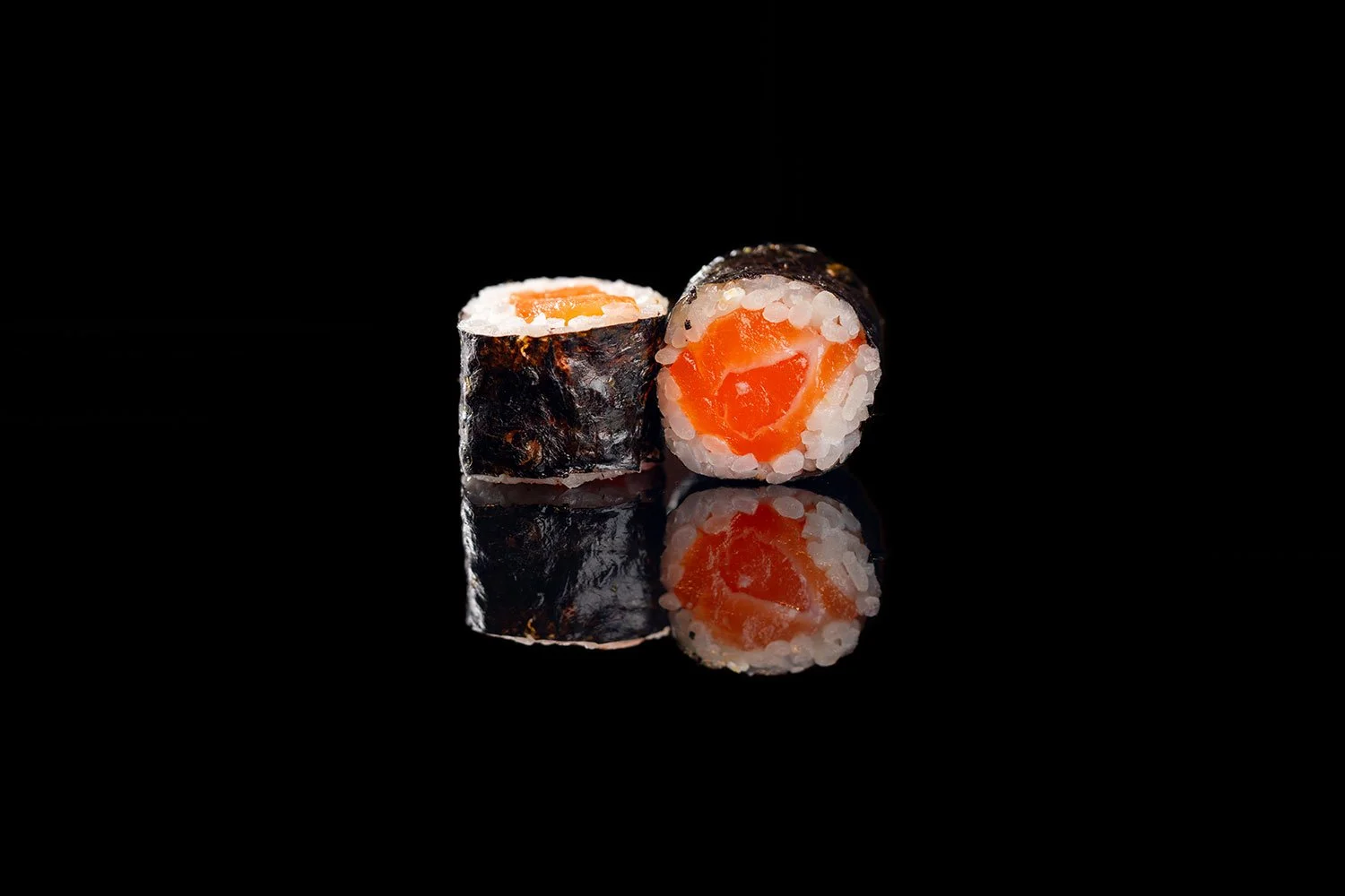 Zwei Sushi-Rollen mit Lachs auf schwarzem Hintergrund, mit Reflexion an der Oberfläche.