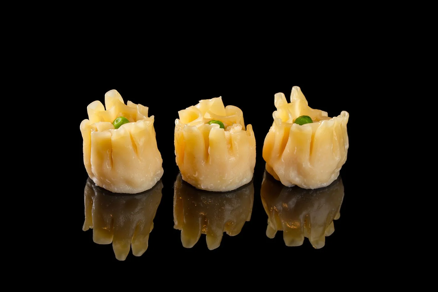 Drei kleine Käse-Schiffchen mit einer grünen Paprika in der Mitte, auf reflektierter schwarzer Oberfläche.