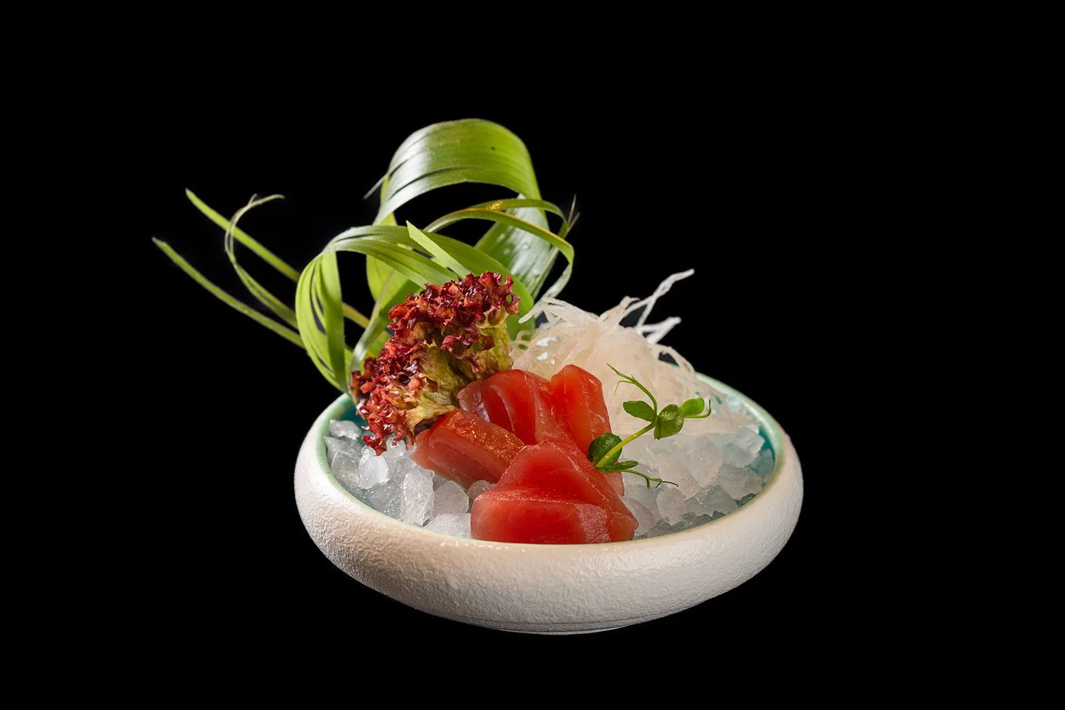 Sashimi mit Lachs, Zwiebeln, Meerrettich, und Dekoration auf Eis in einer weißen Schale, schwarzem Hintergrund.