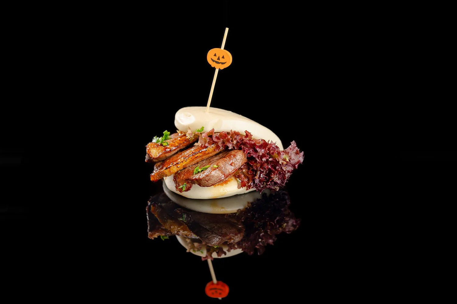 Ein Gourmet-Hamburger mit Rindfleisch, Salat, Röstzwiebeln und Kartoffel in einem Brötchen, mit Halloween-Dekoration auf einem schwarzen Hintergrund.