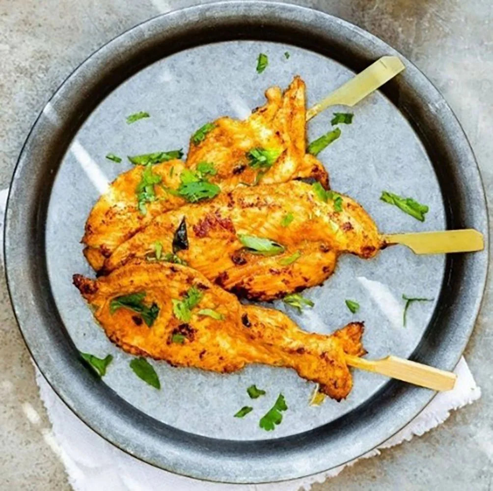 Gegrillte Hähnchenschenkel mit Kräutern auf einem runden, schwarzen Teller