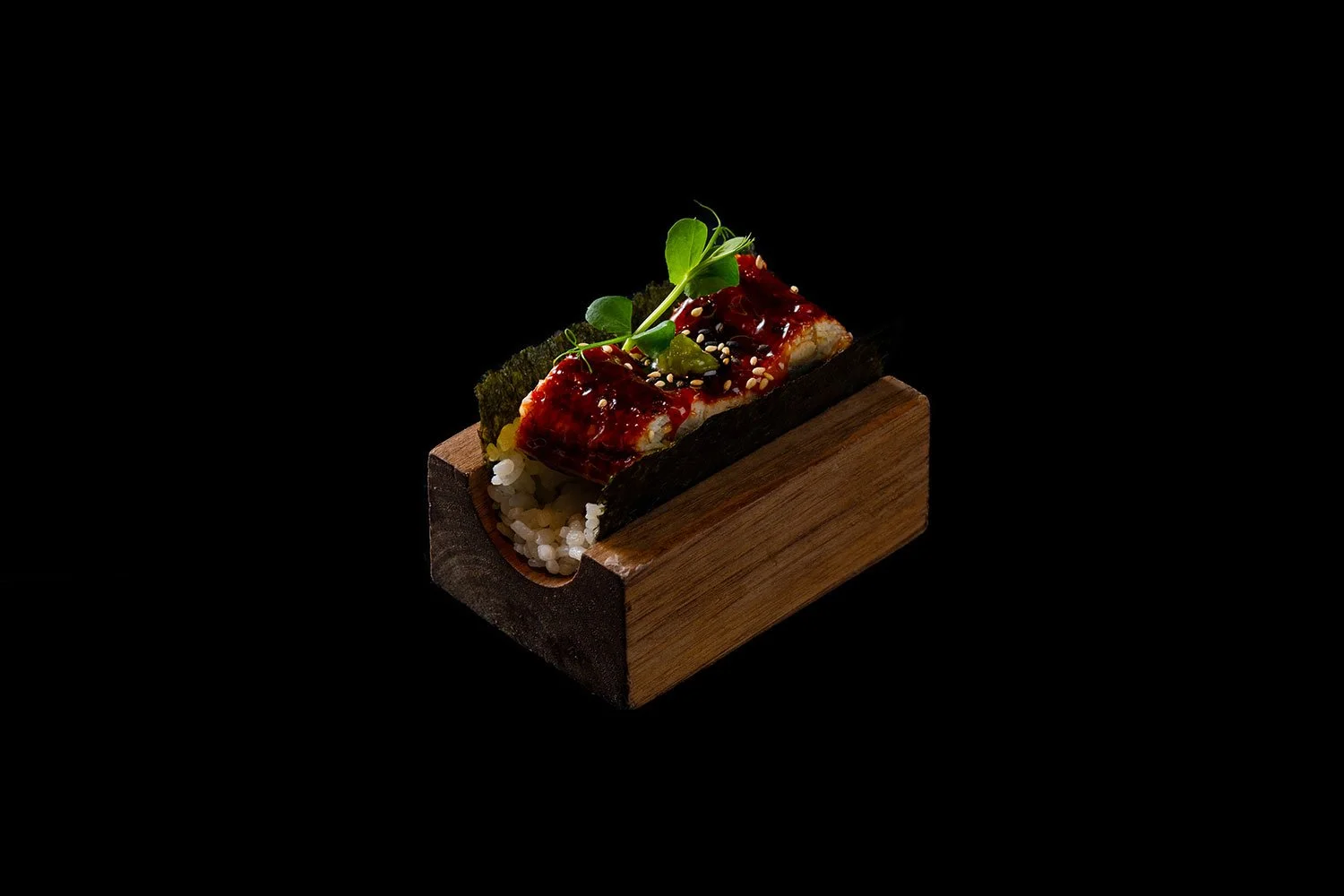 Sushi auf Holzblock serviert, mit Tomaten- oder roten Chilisauce, Sesam, grünen Kräutern und Meerespflanzen auf schwarzem Hintergrund.