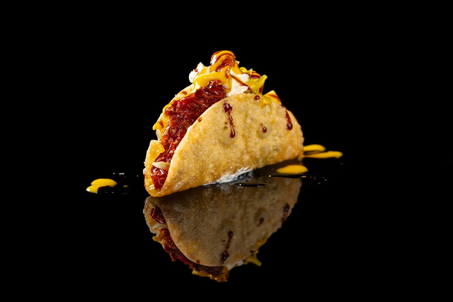 Ein Taco mit rotem Fleisch, Zwiebeln, Sauce, und yellowem Sauce auf schwarzem Hintergrund