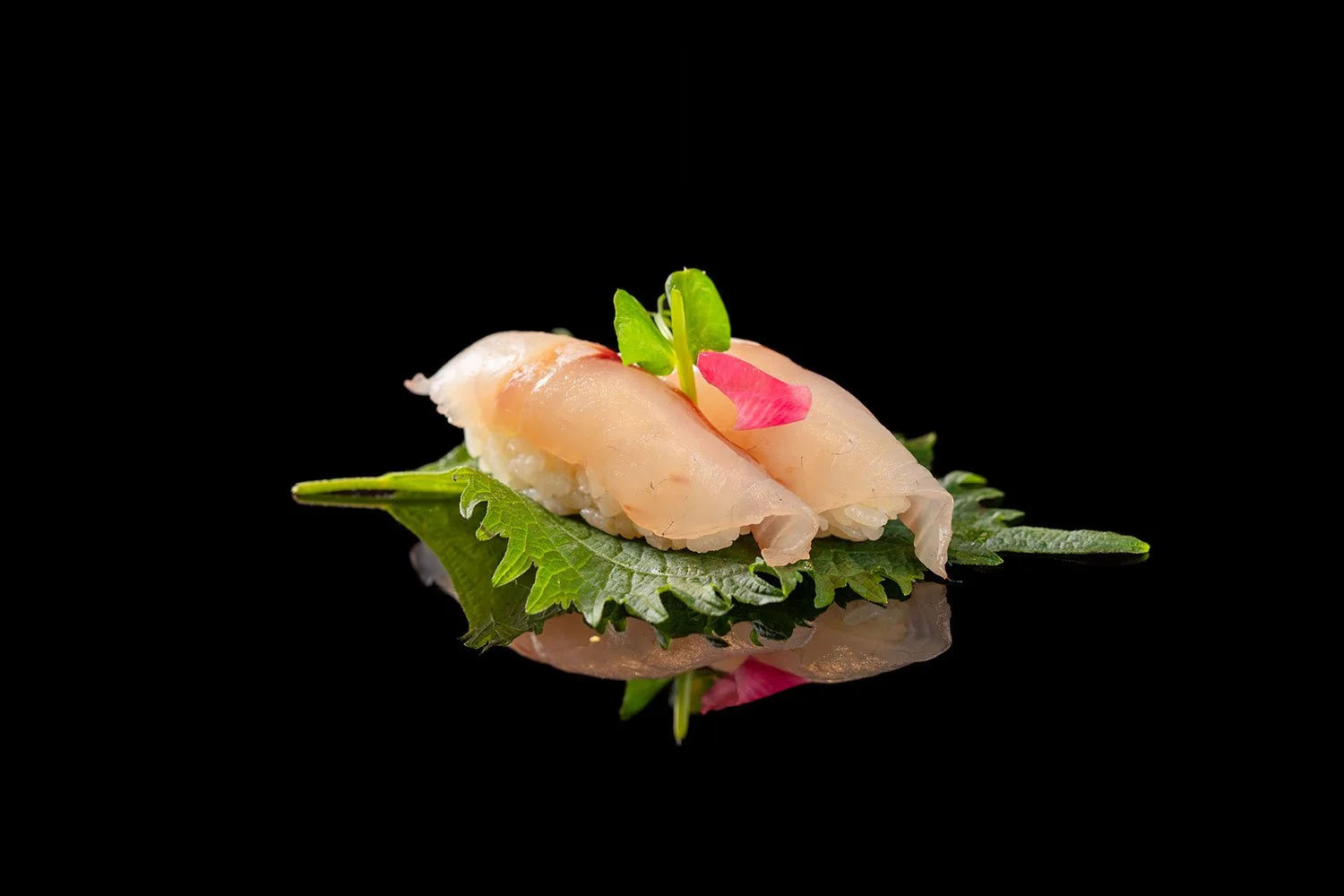 Sushi mit Fisch auf einem grünen Blatt, Deko mit kleinen Blättern und Blüten, auf schwarzem Hintergrund