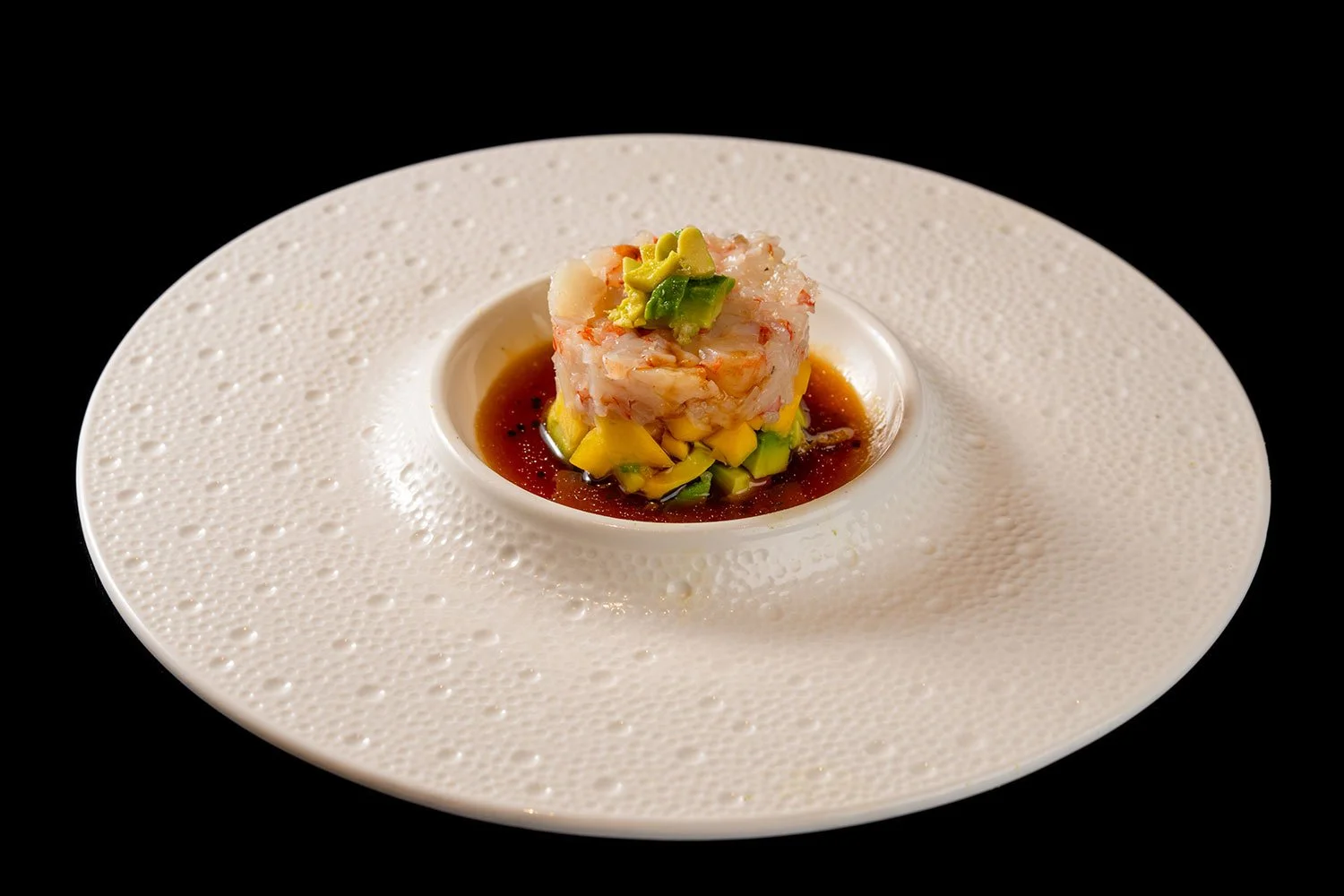 Feines Sushi mit Avocado und einer Soße auf einem dekorativen weißen Teller gegen schwarzen Hintergrund.