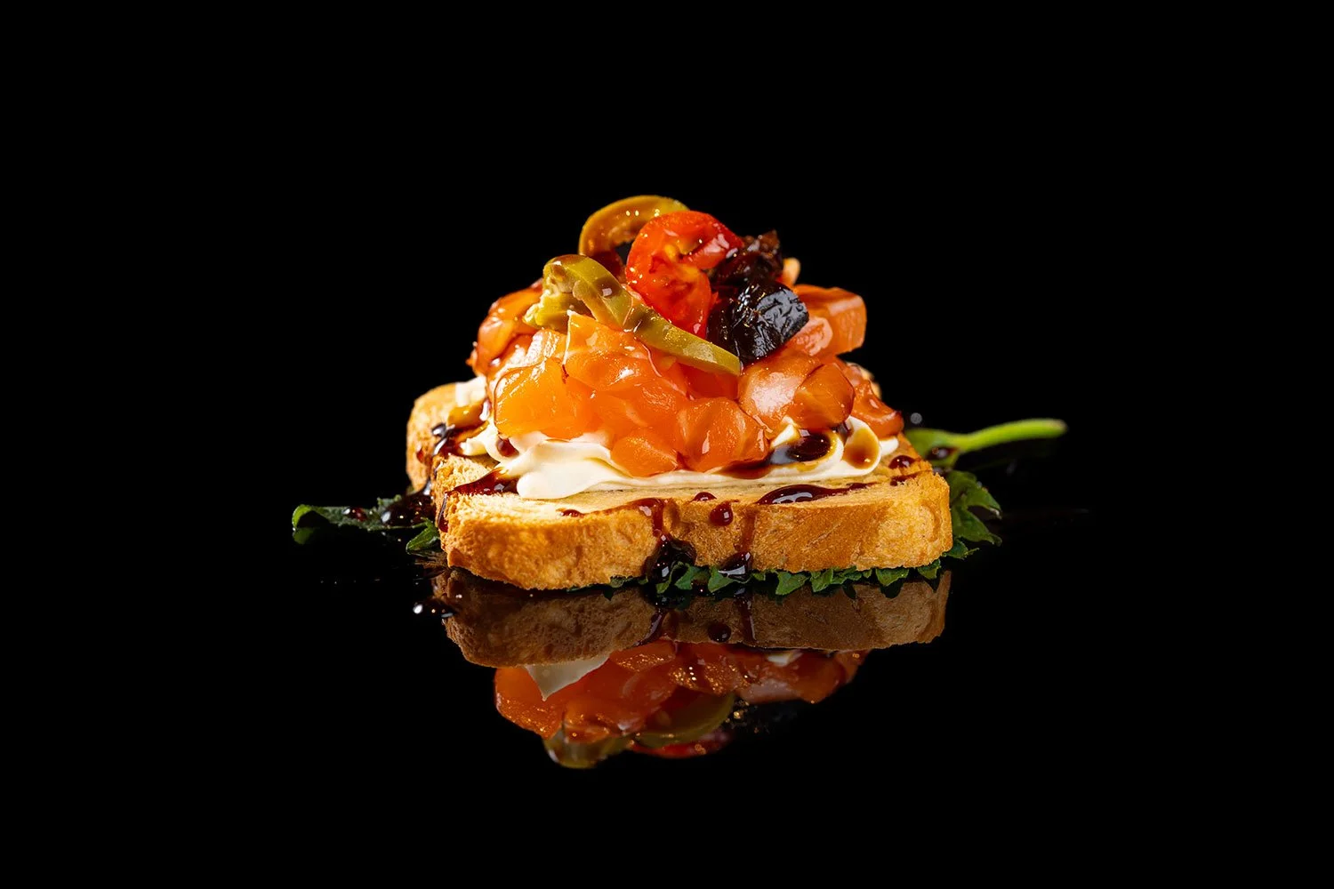 Ein belegtes Brot mit Lachs, Tomaten, Oliven und Sprossen auf schwarzem Hintergrund.