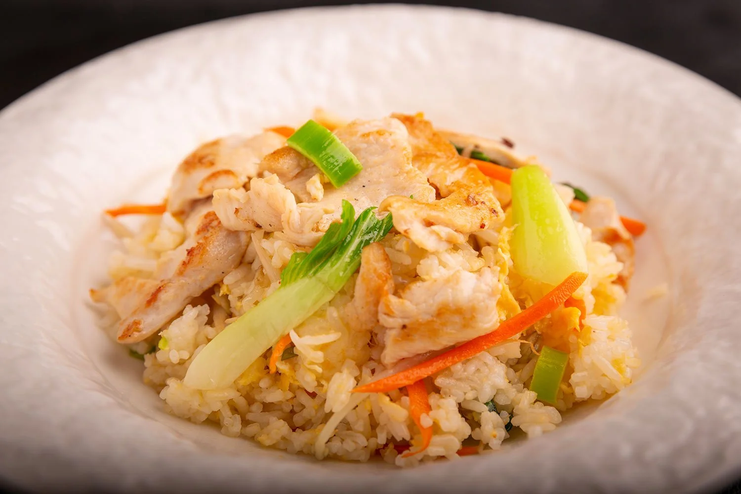 Hähnchen-Reis mit Frühlingszwiebeln, Karotten und Ei in einer weißen Schüssel.