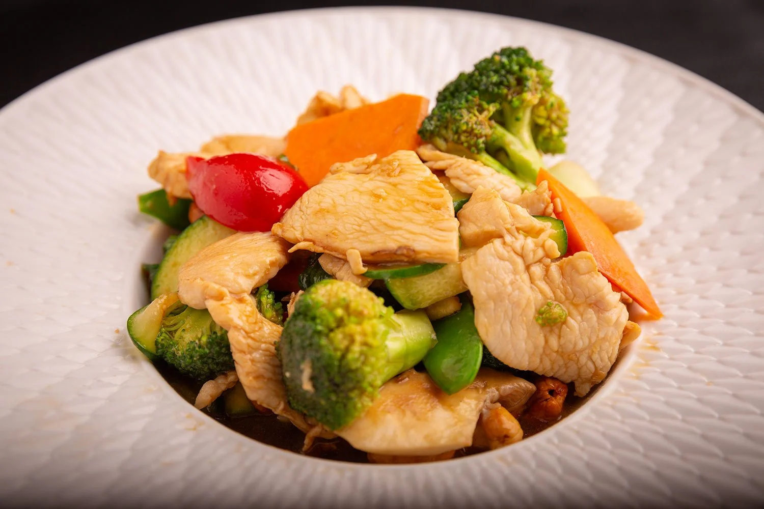 Gemüsepfanne mit Brokkoli, Karotten, Zucchini, Cherry-Tomaten und Hähnchenstücken auf einem weißen Teller