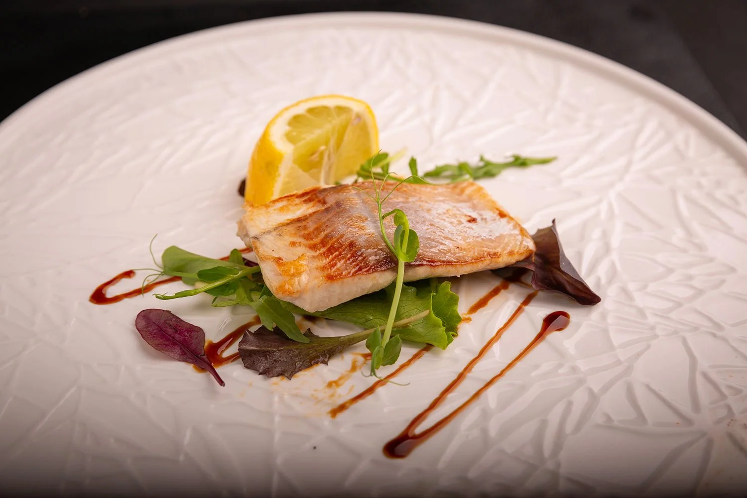 Gegrilltes Fischfilet mit Salat, Zitrone und Balsamico-Sauce auf weißem Teller