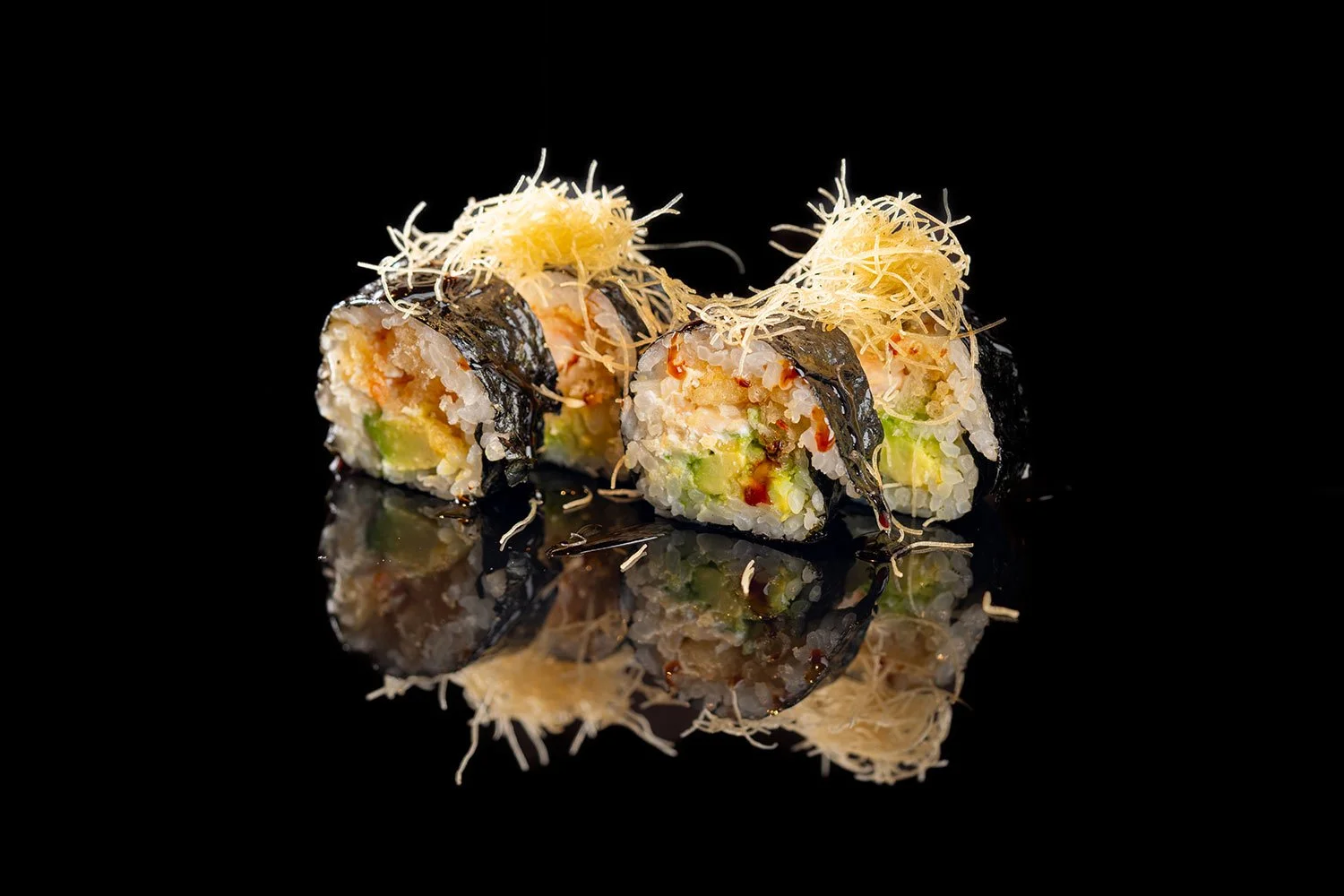 Nahaufnahme von Sushi-Rollen mit Nori, Reis, Avocado, Garnelen, und Parmesan auf schwarzem Hintergrund, mit Reflexion.