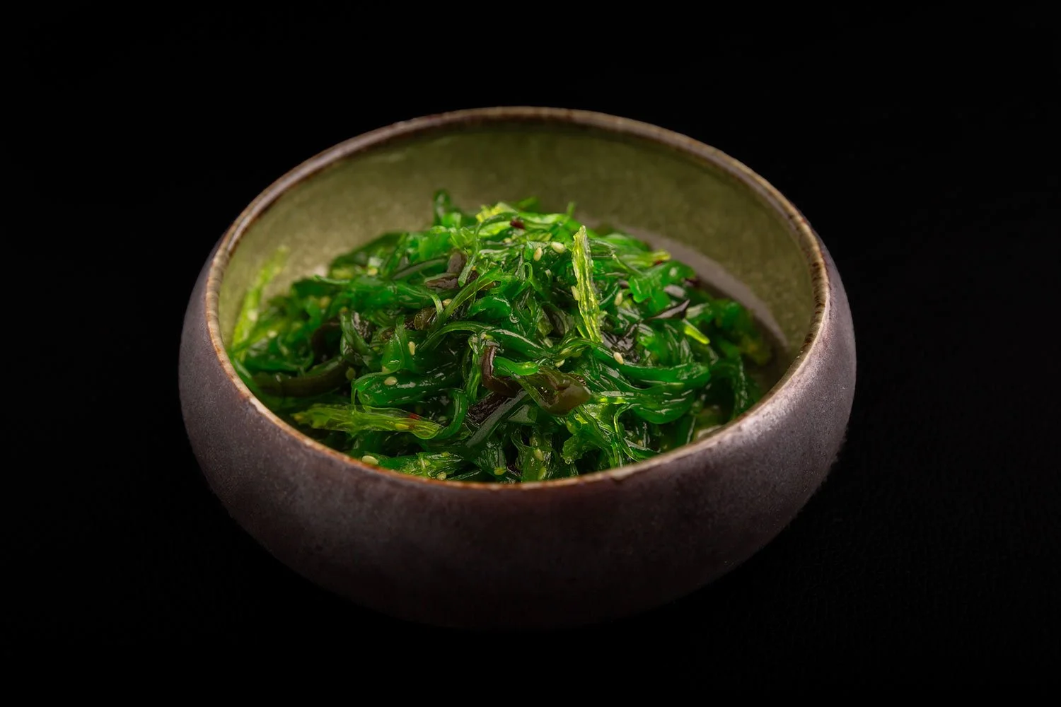 Grüner Seetang in einer grünen Keramikschale auf schwarzem Hintergrund