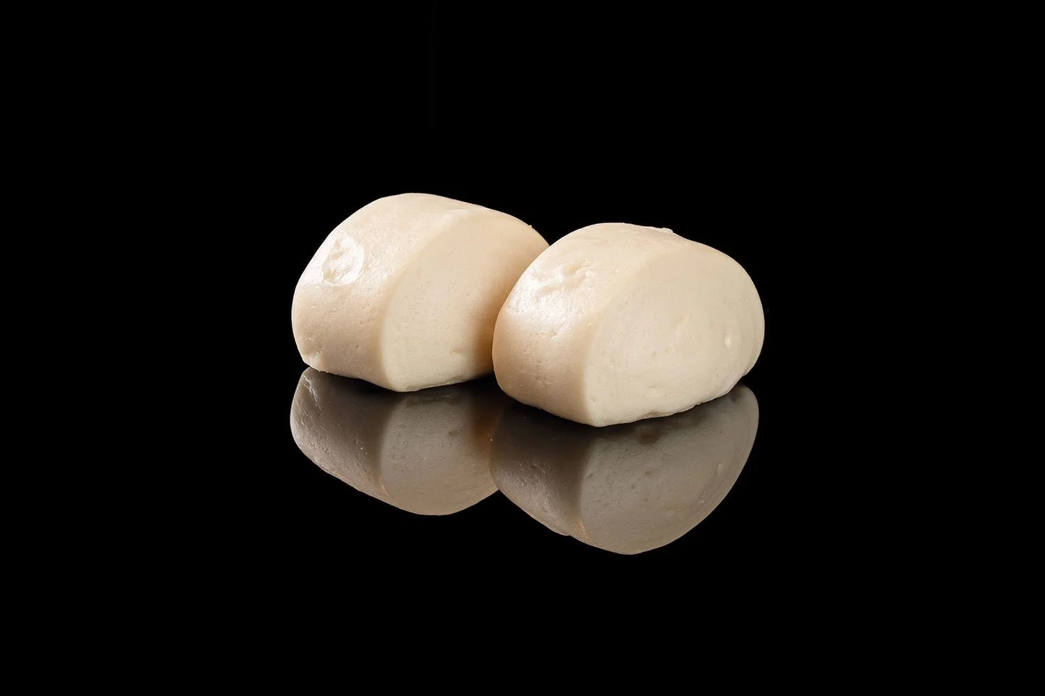 Zwei Scheiben Mozzarella-Käse auf einer schwarzen reflektierenden Oberfläche gegen schwarzen Hintergrund.