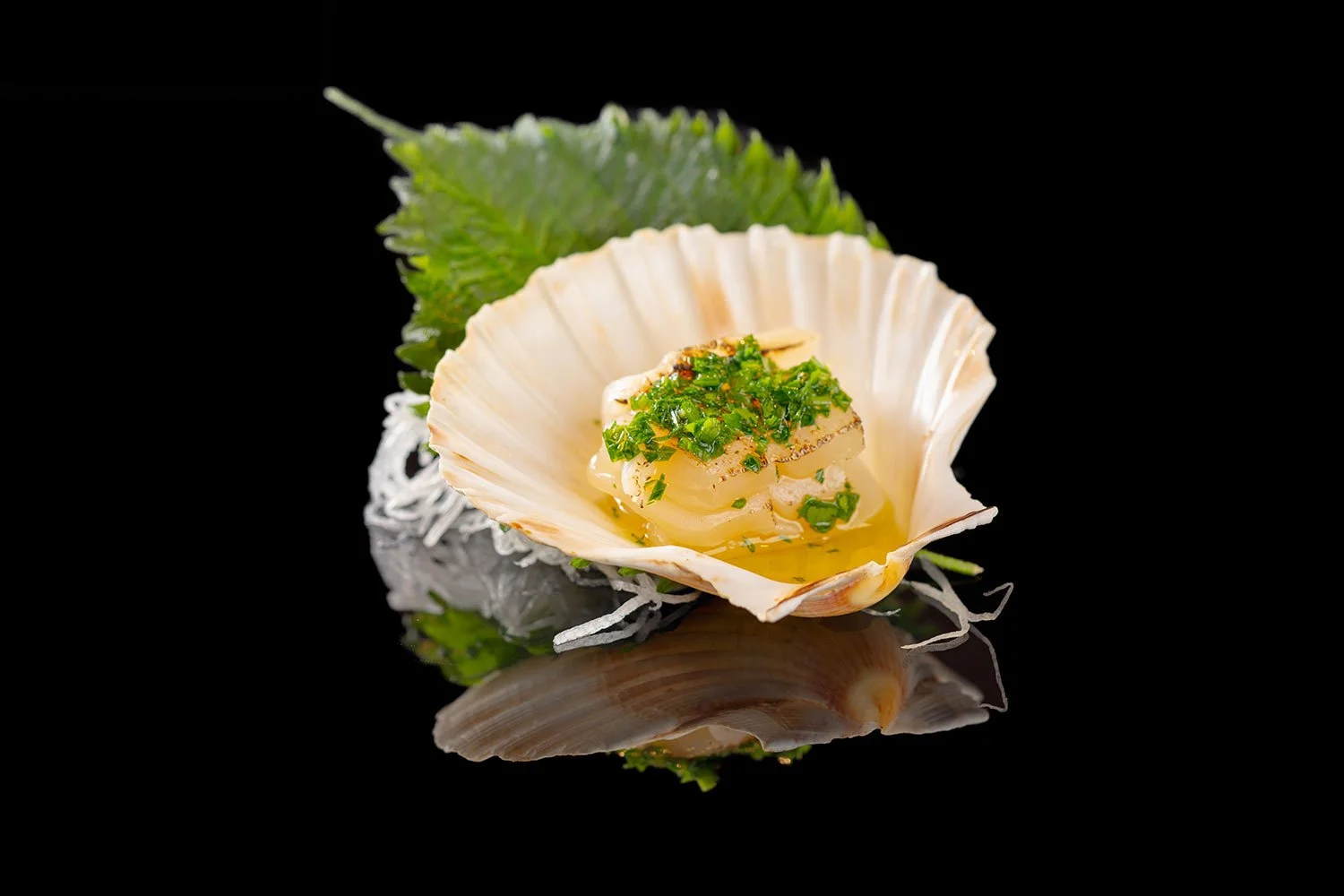 Muschel mit einer cremigen Fischfüllung, garniert mit gehackten grünen Kräutern, auf einem schwarzen Hintergrund mit Spiegelung.