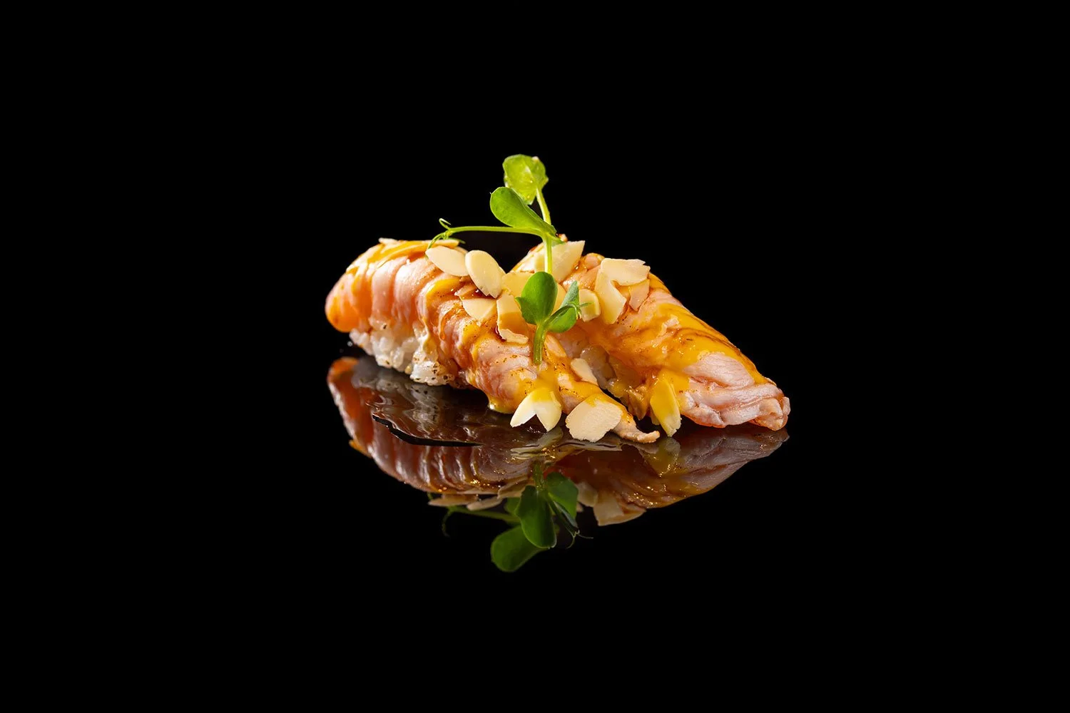 Garnierte Sushi mit Lachs, Alfalfa, Mandelsplittern und Honig auf schwarzem Hintergrund mit Reflexion