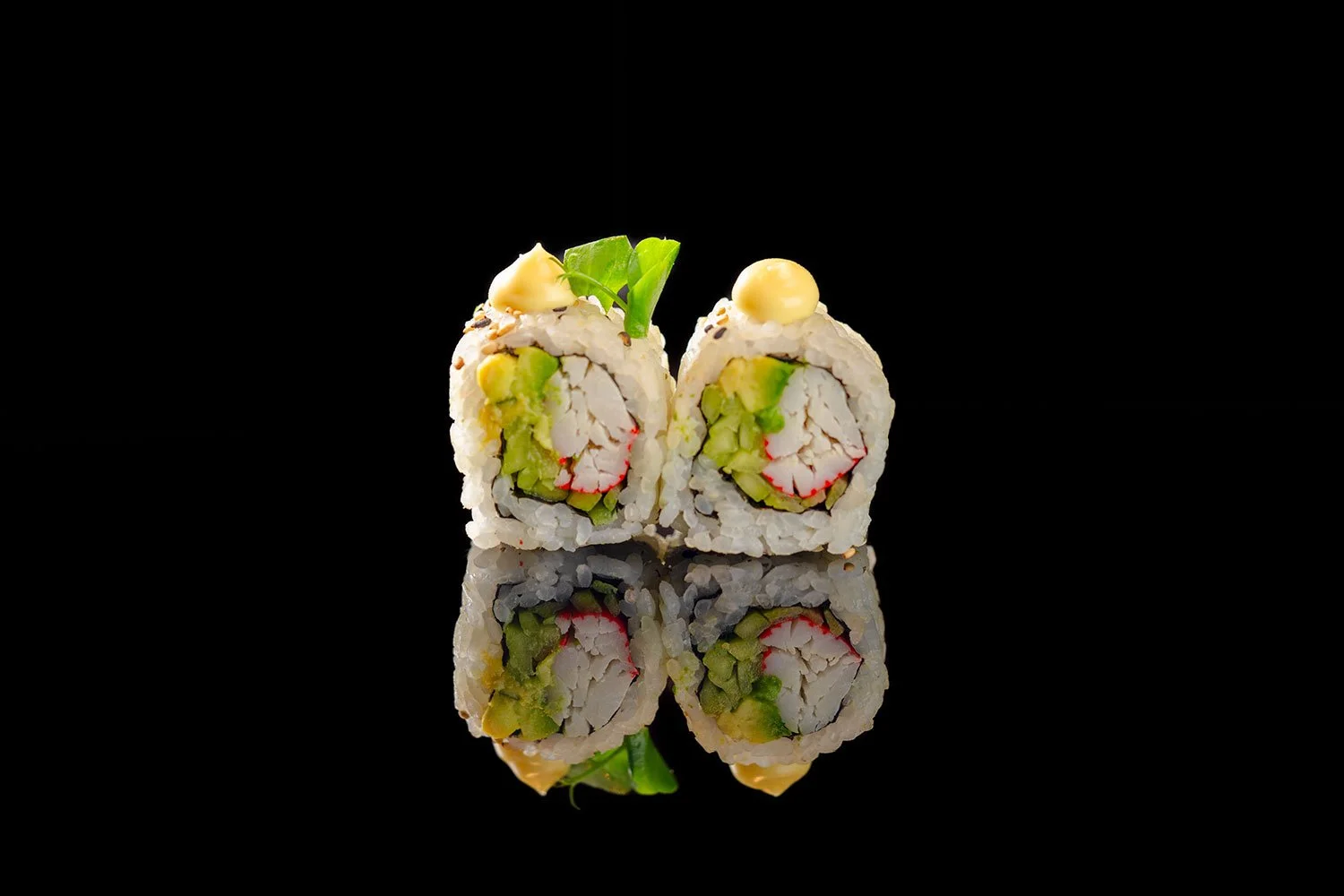 Zwei Sushi-Rollen mit Gurke, Krabbe und Reis, dekoriert mit Mayonnaise und wasabi, auf schwarzem reflektierendem Hintergrund.