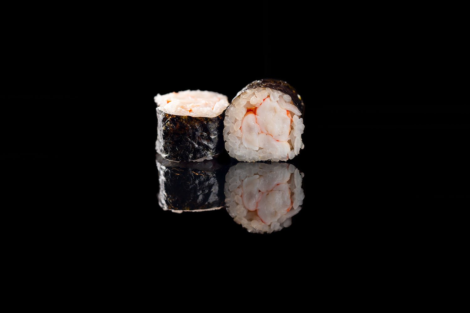 Zwei Sushi-Rollen mit Shrimp-Füllung vor schwarzem Hintergrund, mit Spiegelung auf der Oberfläche.